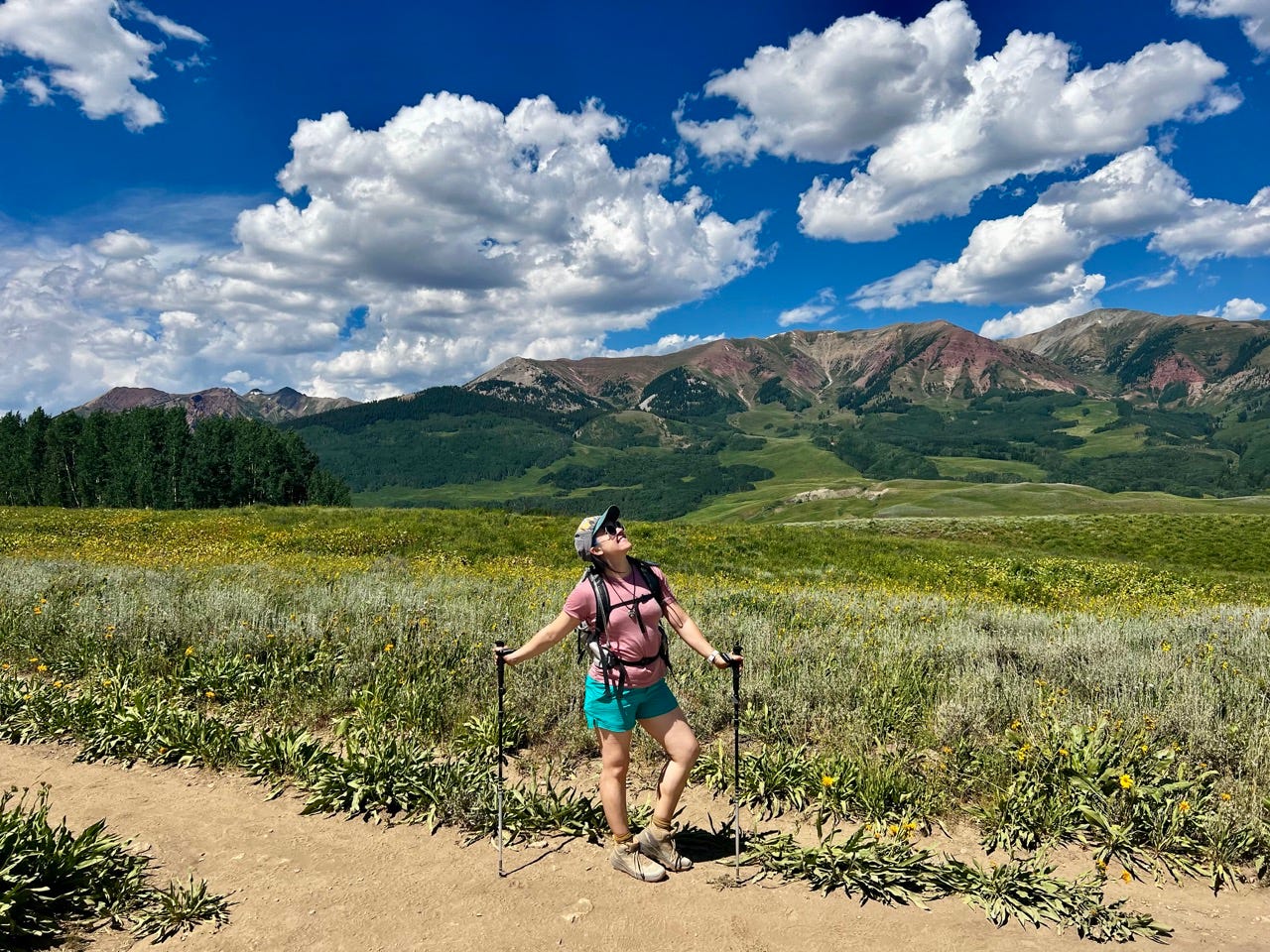 Author Emily Pennington posing among wildflowers, mountains, and field in Crested Butte