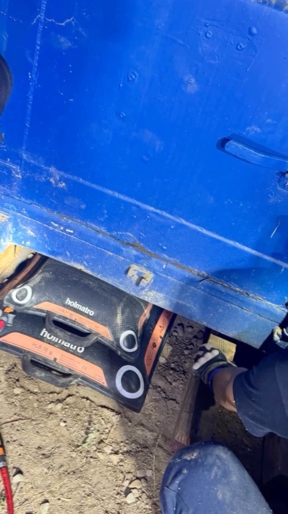 Person working on holmatro hydraulic equipment under a blue machine.