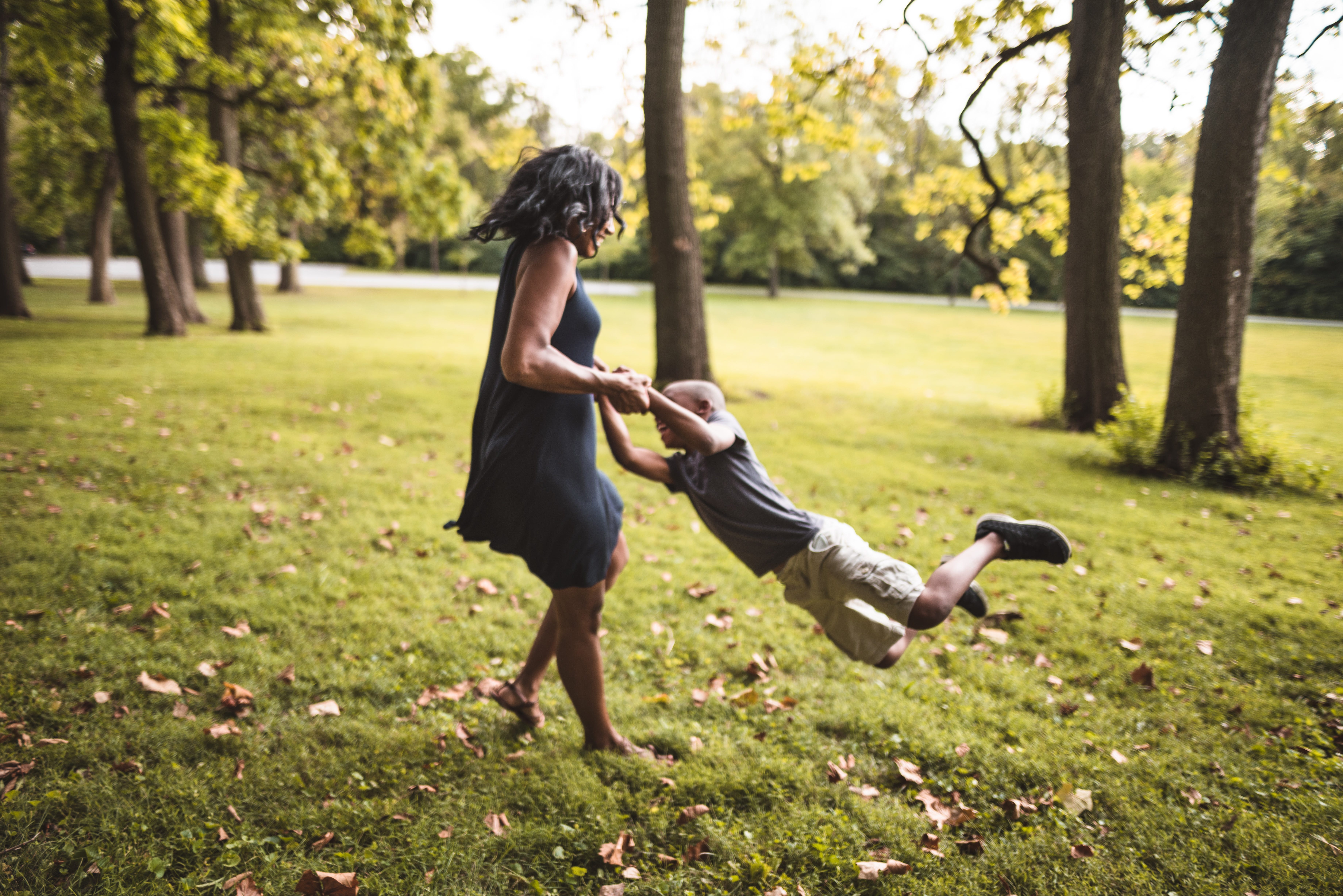 A mother flings her son around while playing in a park.