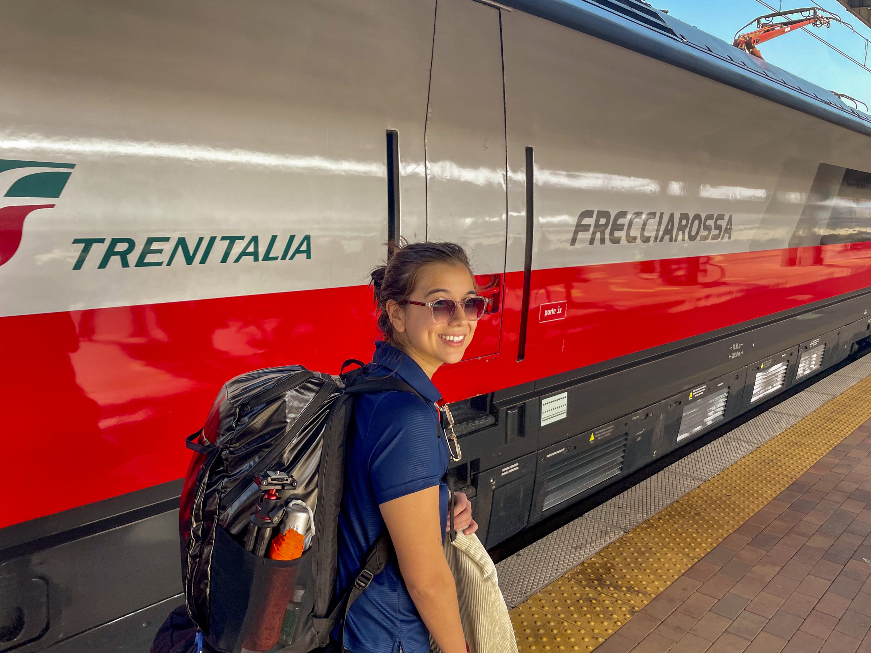 The author stands with a backpack on in front of a train in Italy