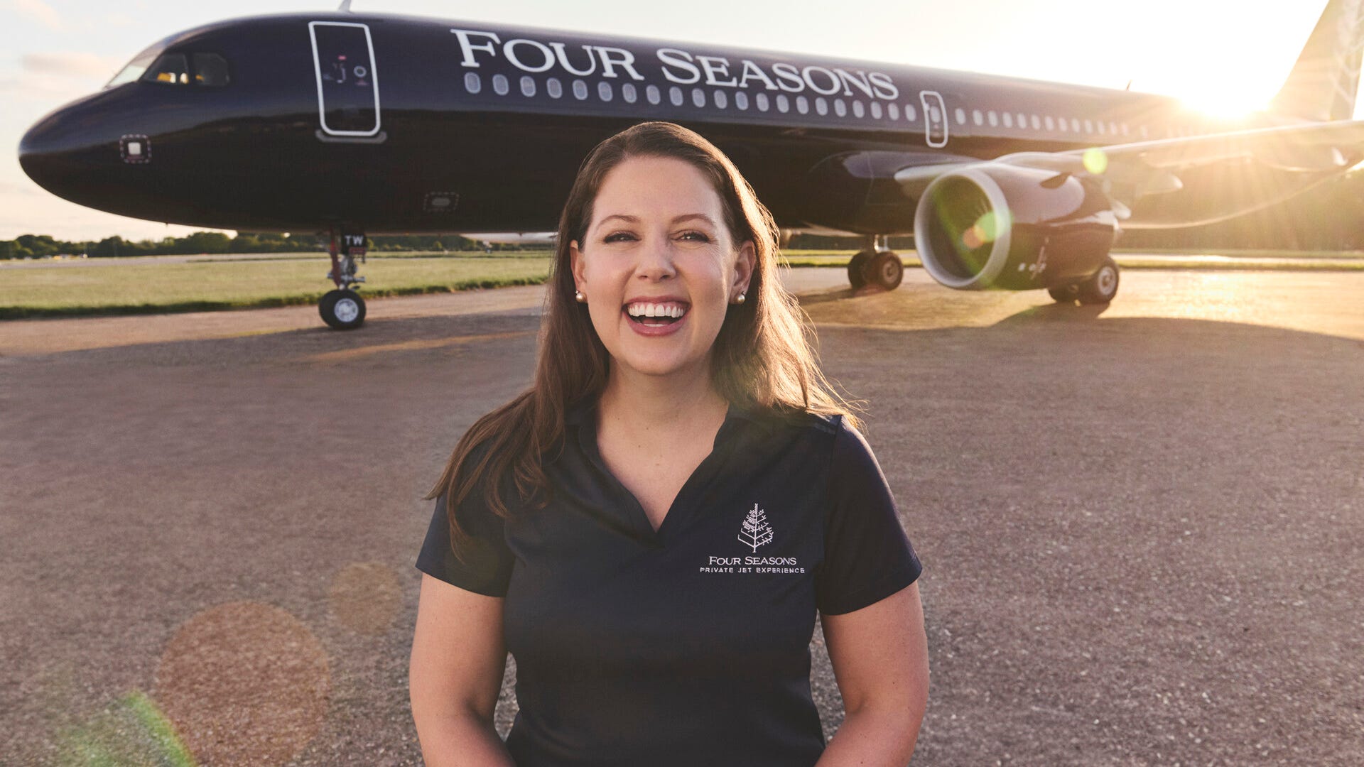 Chenin Matthews, Director of Guest Experience for the Four Seasons Private Jet, wearing a company polo shirt and standing in front of the company's Airbus A321LR private jet.