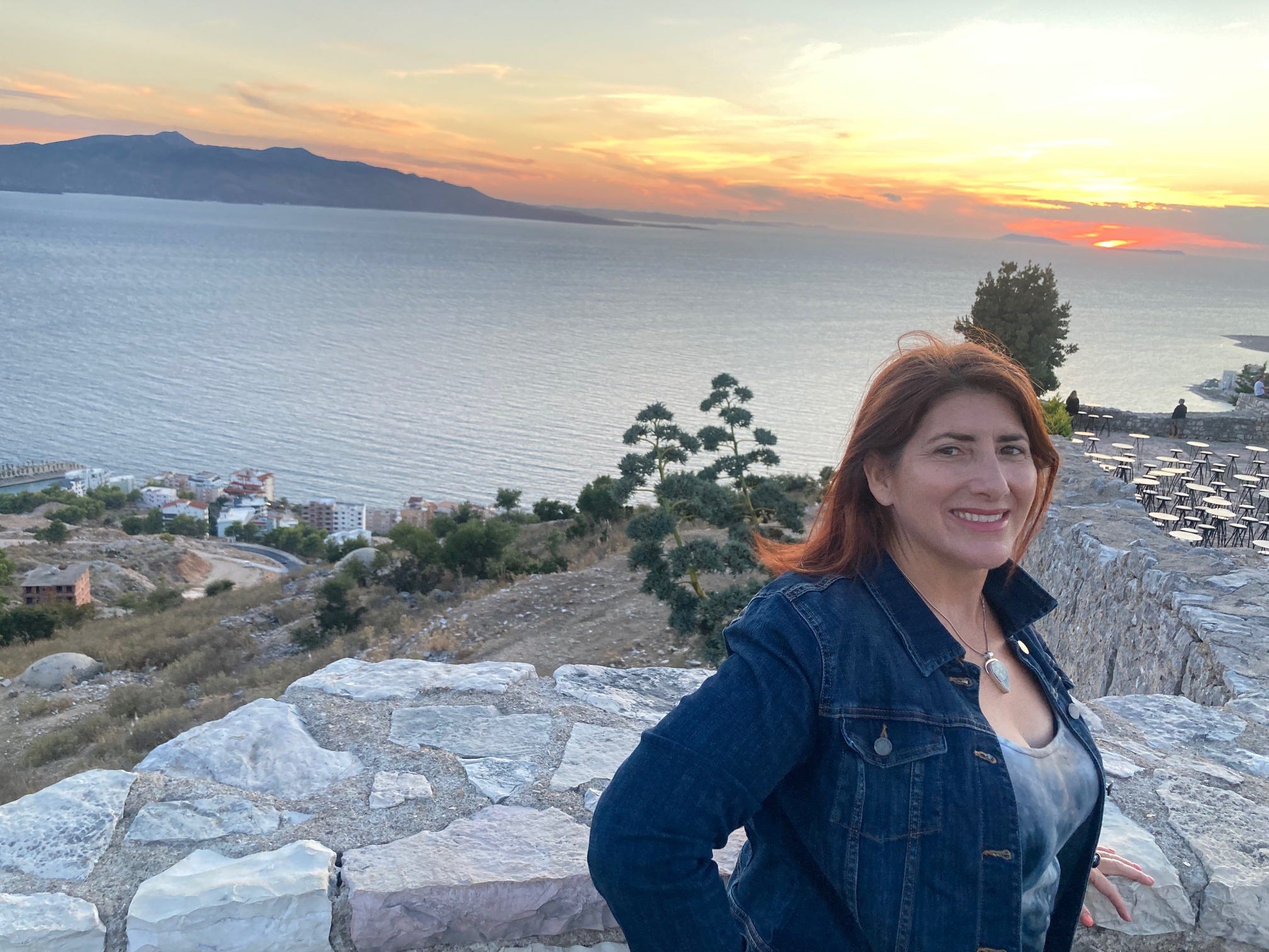 Orlov standing on top of a hill, overlooking an Albanian city, with the sun setting in the back.