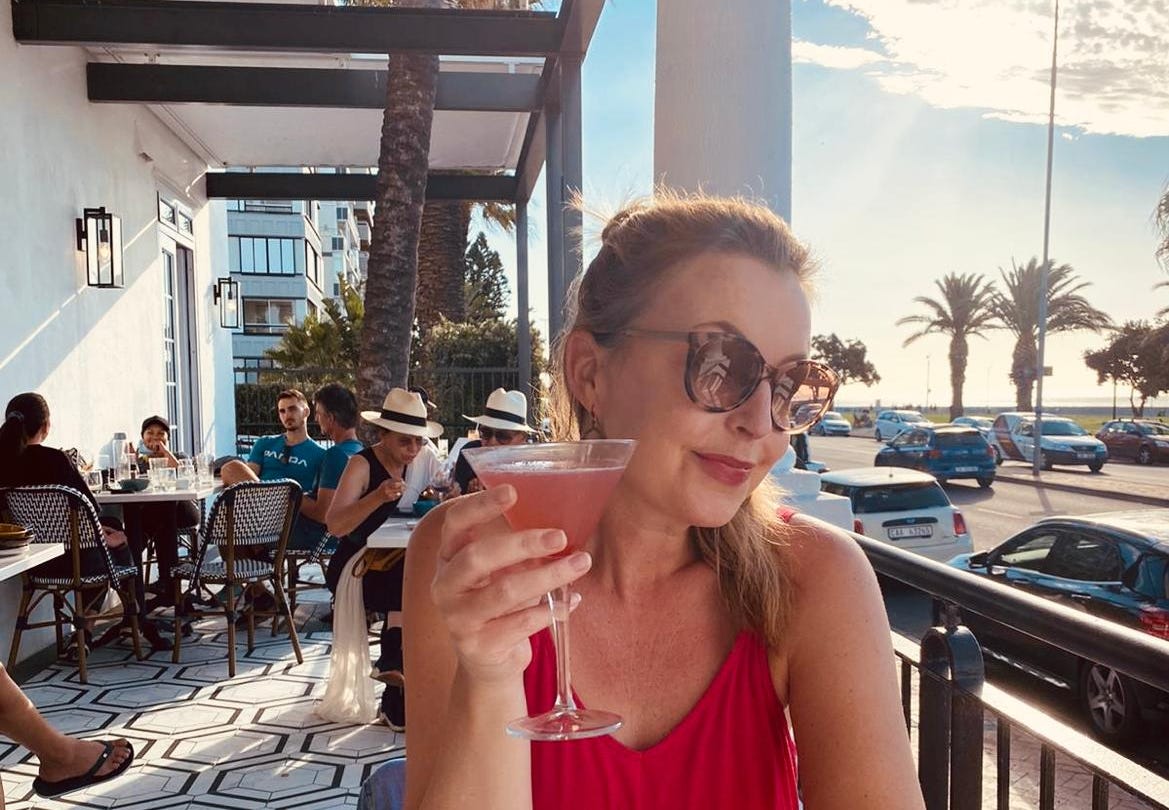 woman in pink shirt holding a pink cocktail in a tropical setting