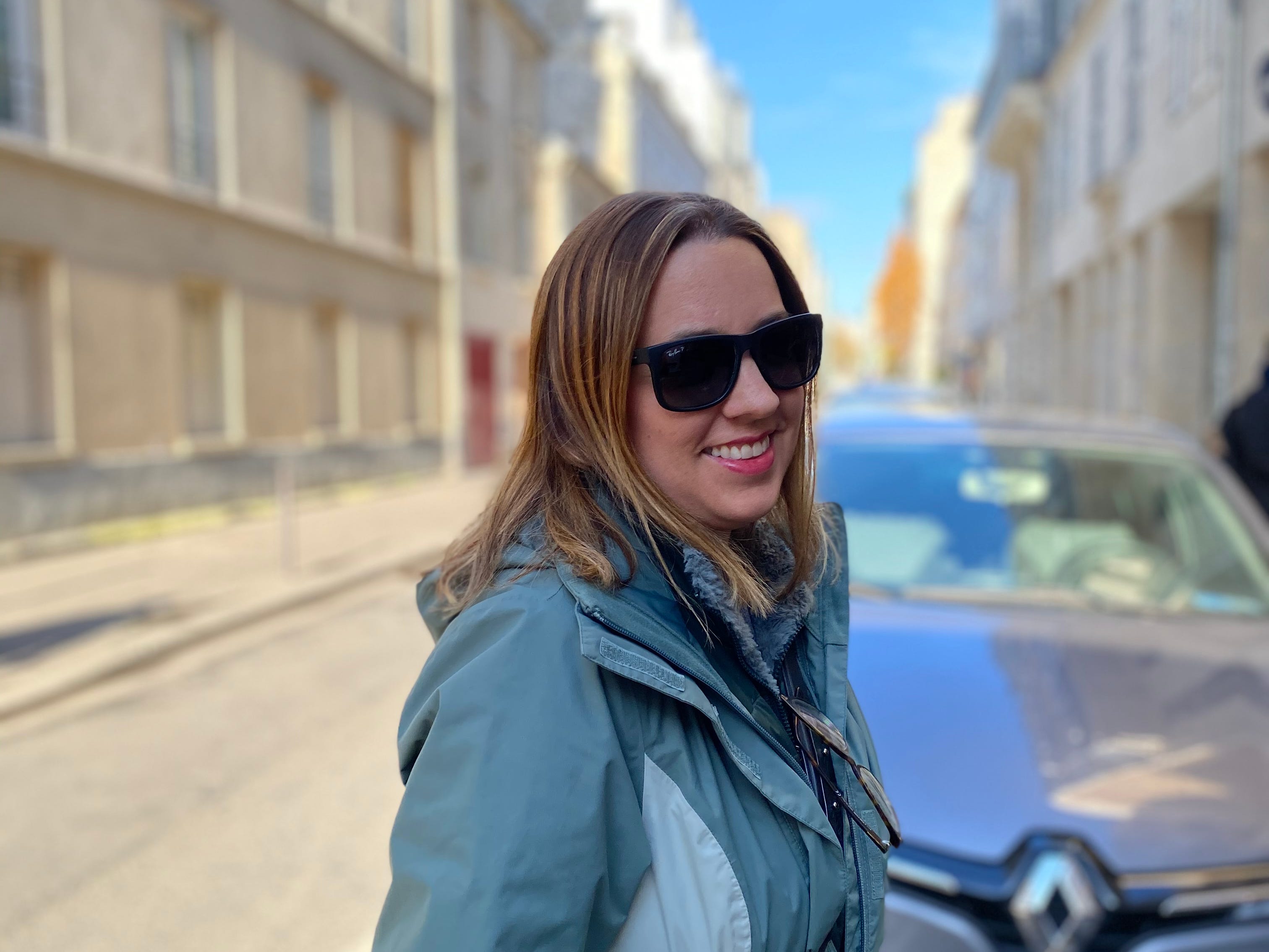 woman in blue coat and sunglasses smiling at camera