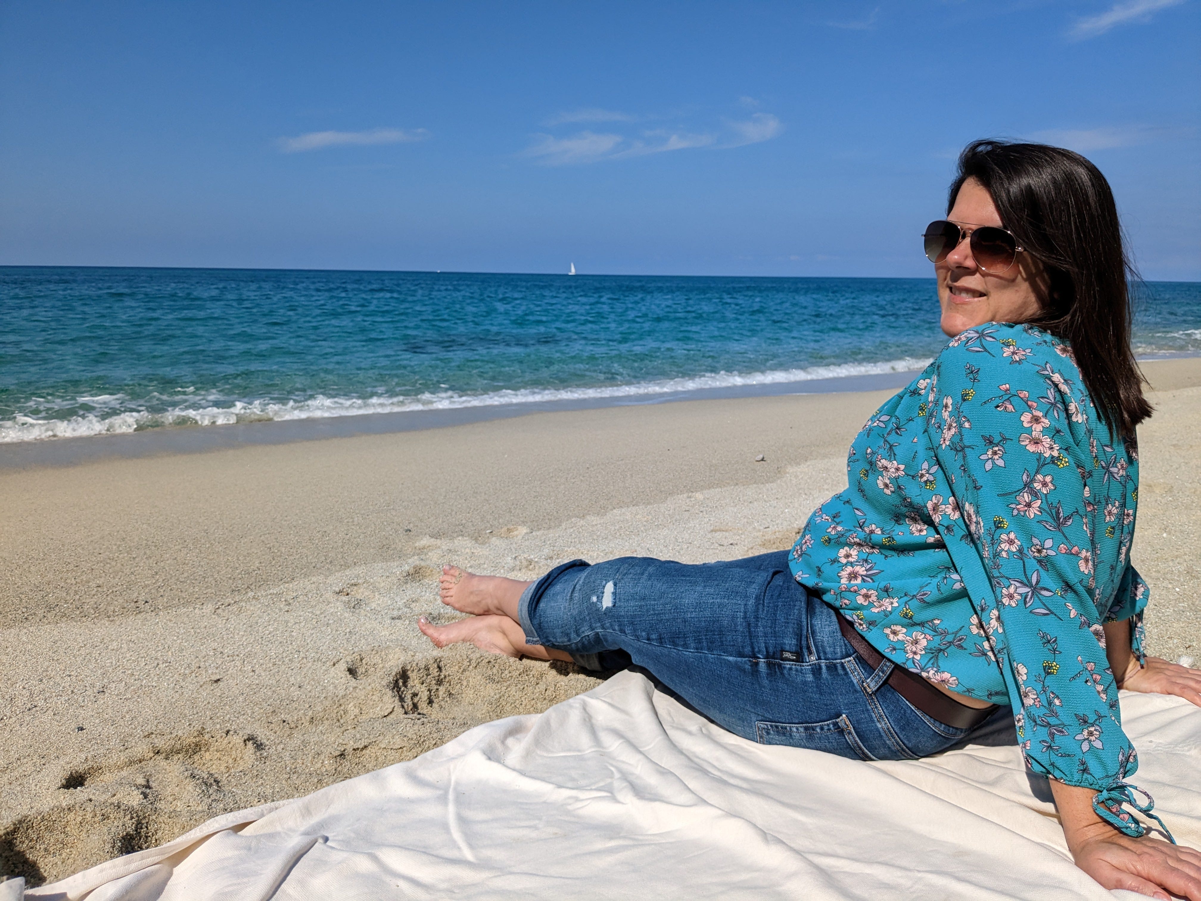 Woman on beach in jeans and a blue flower shirt.
