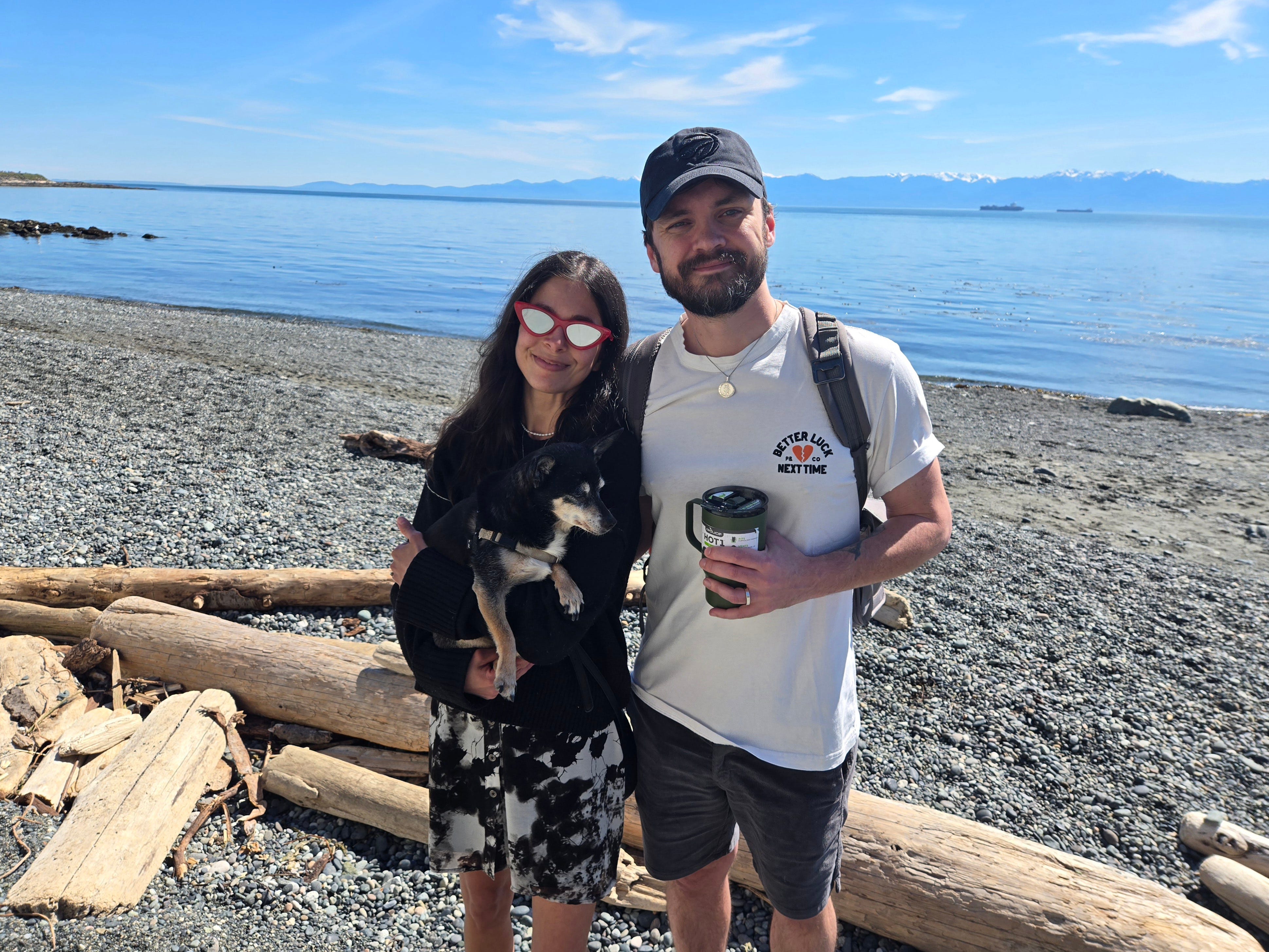 Author Maria Polansky holding a dog and smling with her partner on a beach