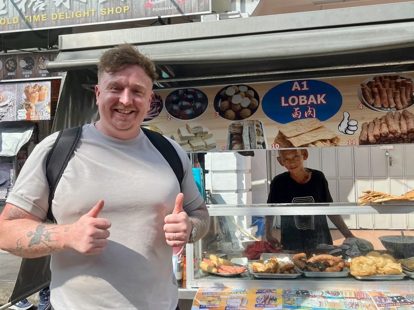 A man posing in front of a street hawker in Malaysia.