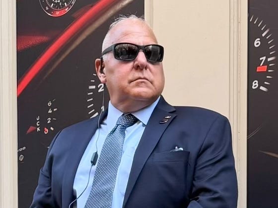 A security guard in sunglasses and a suit standing in front of a building