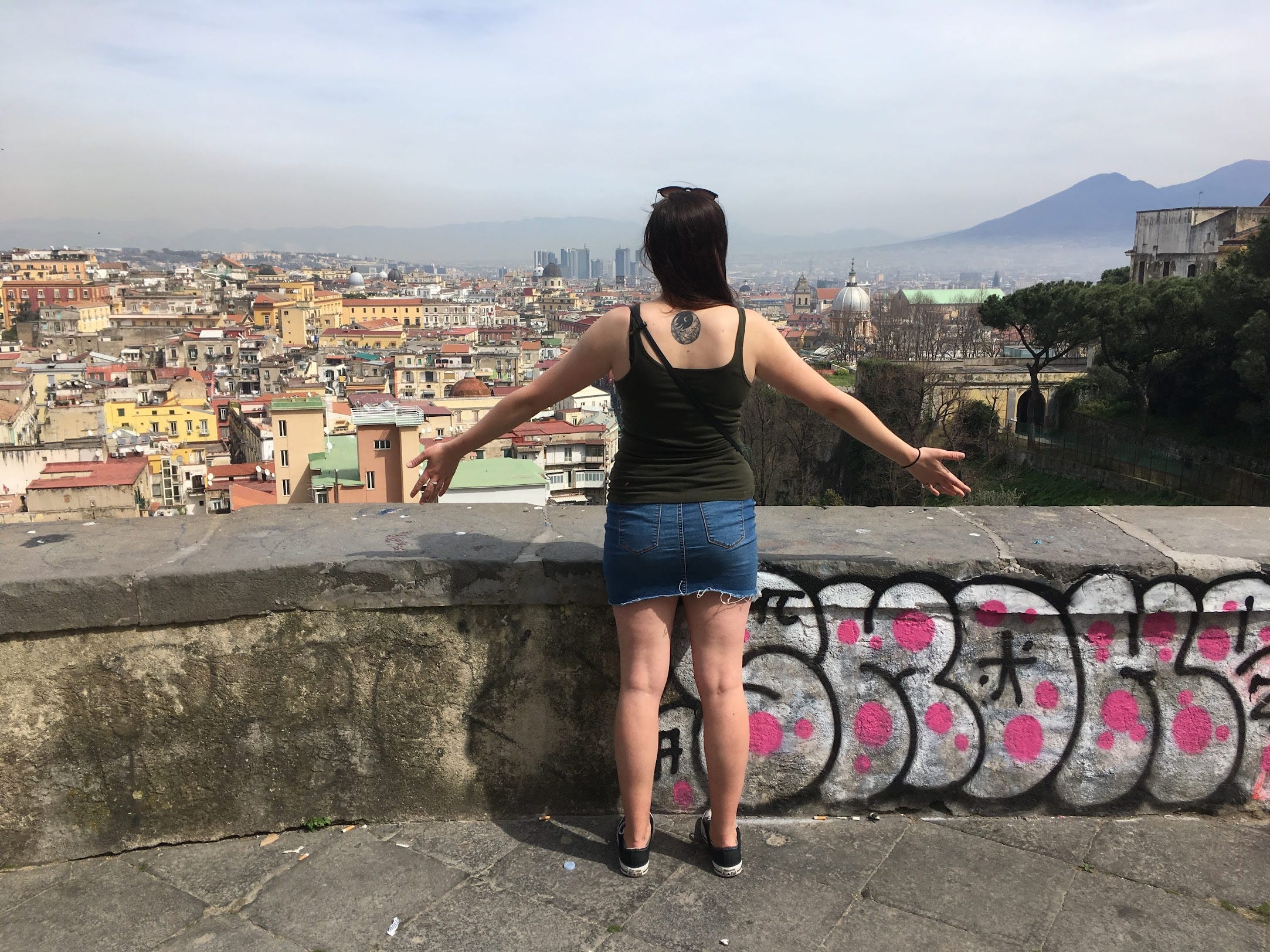 woman in jean skirt and black tank standing in front of naples, italy
