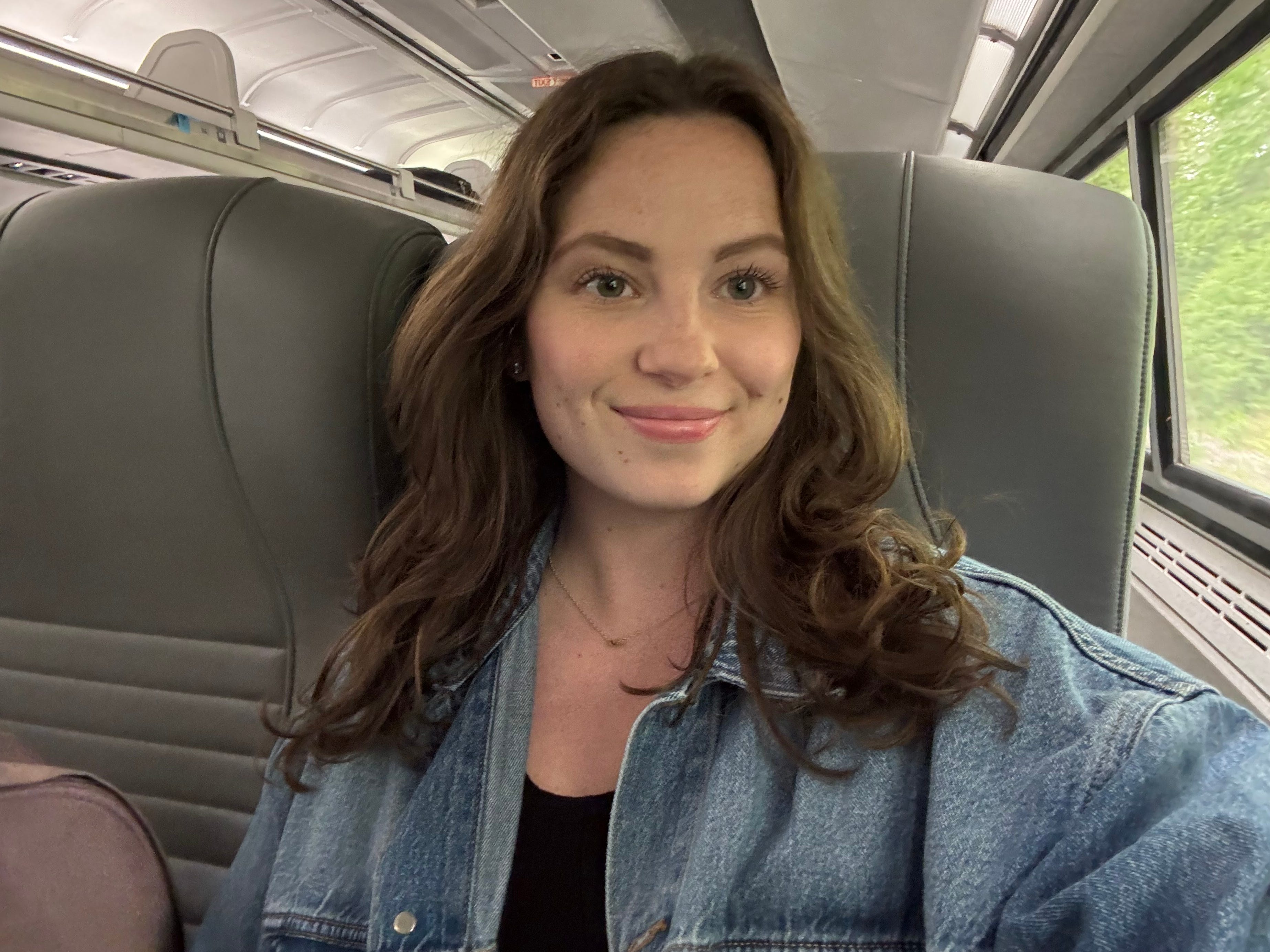 A selfie of a woman sitting on an Amtrak train with gray seats.