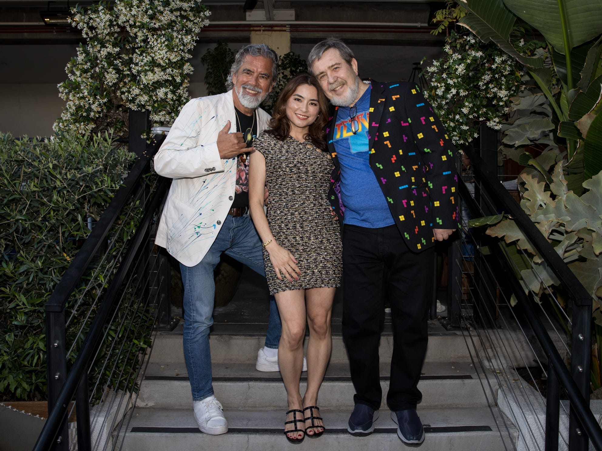 Henk Rogers, Maya Rogers, Alexey Pajitnov smiling and standing on a set of steps.