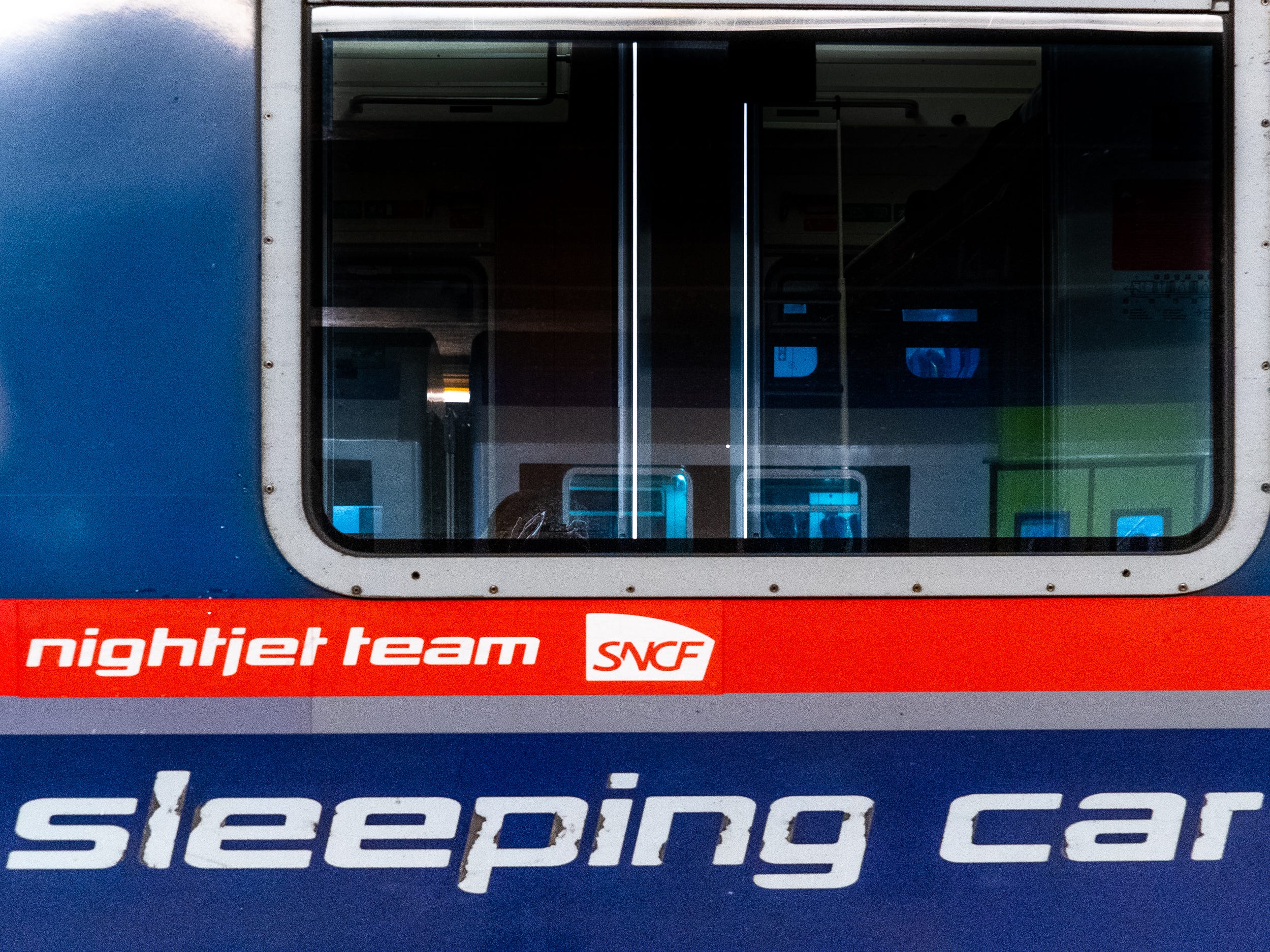 The outside of a blue train sleeping car with a red stripe with a window.