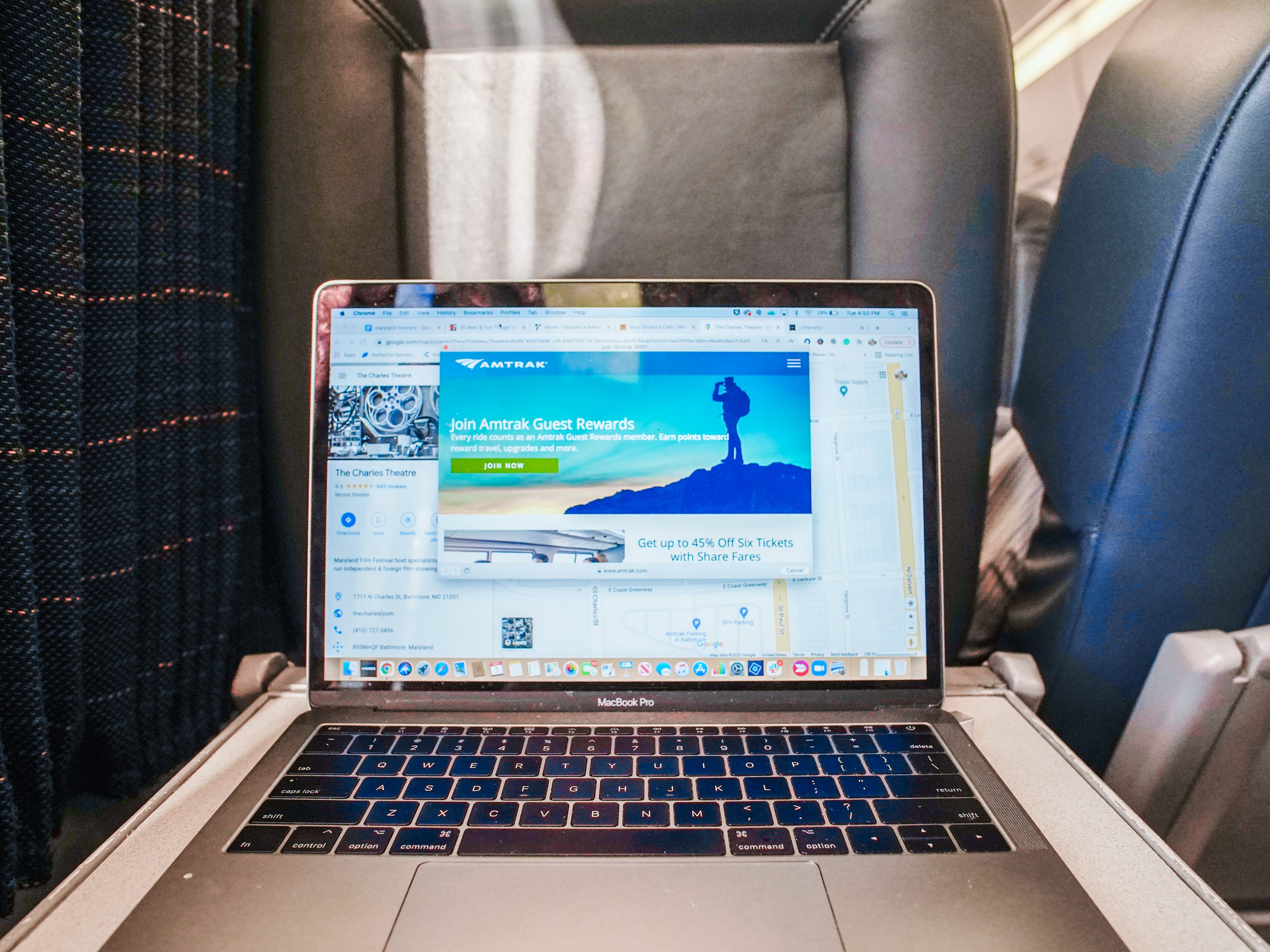 A MacBook opened on a tray table in a business-class Amtrak Acela train car