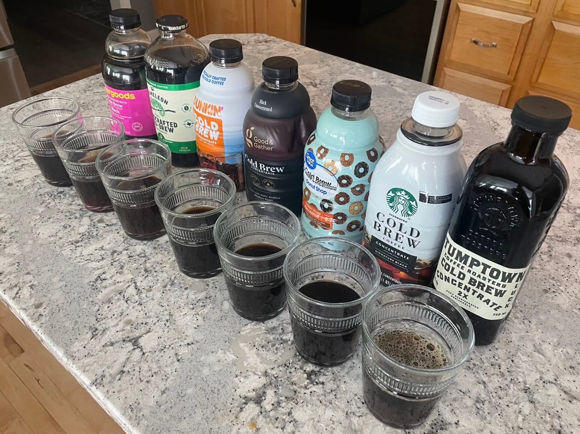 Cold bre concentrate bottles lined up on counter with glasses of cold brew in front of each
