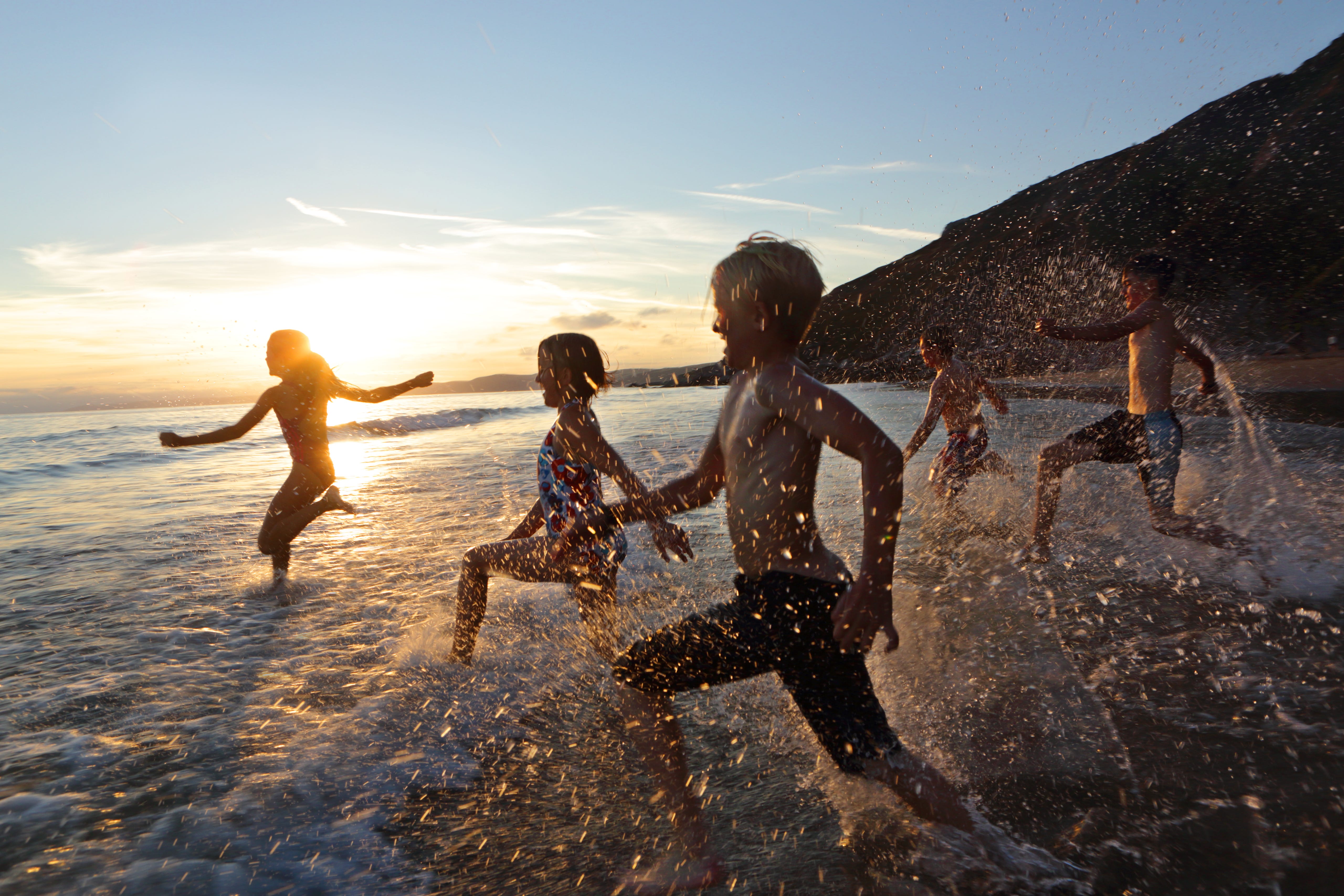 Children running into sea at sunset