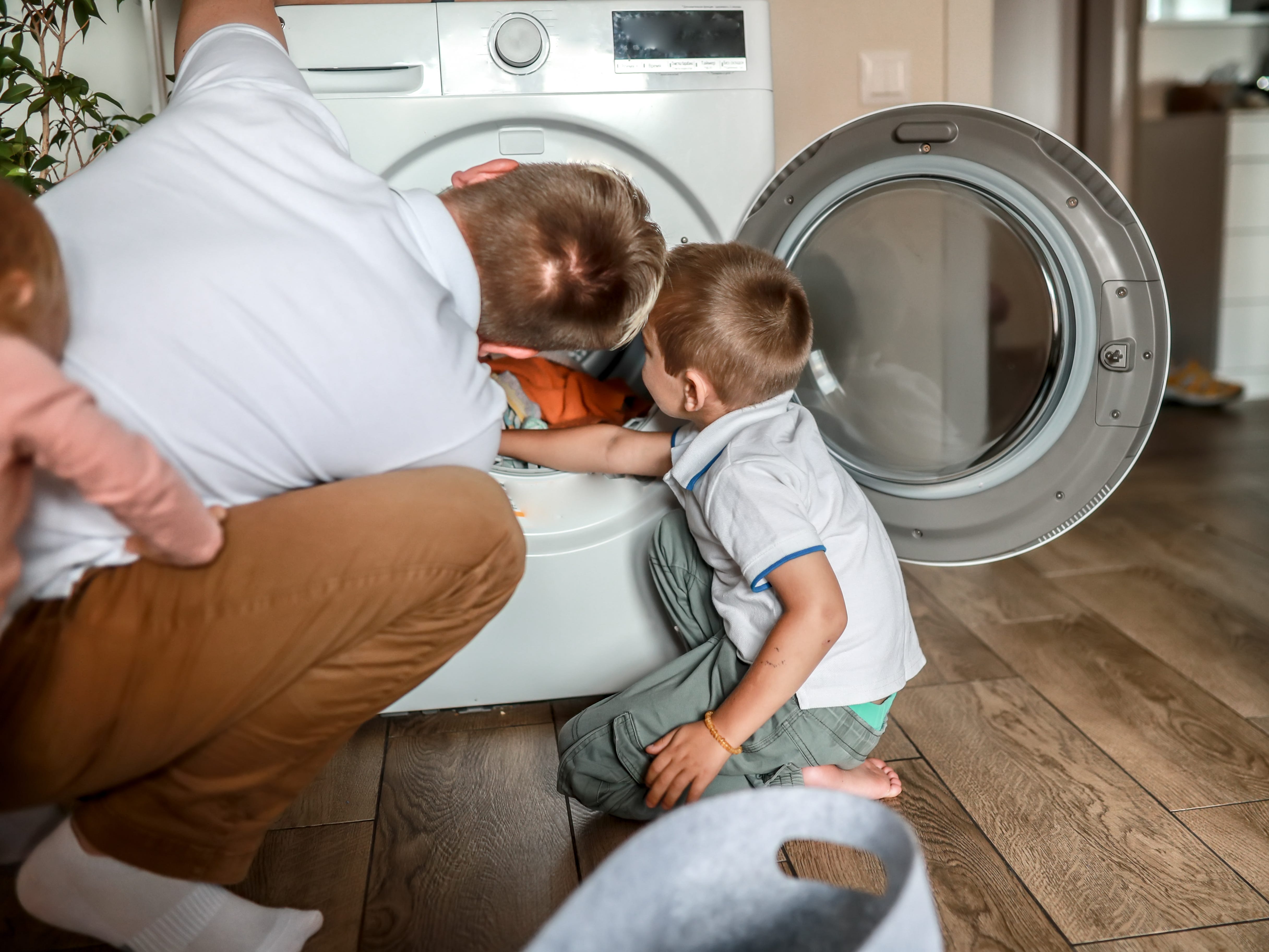 A dad with his two kids in front of a washing machine.