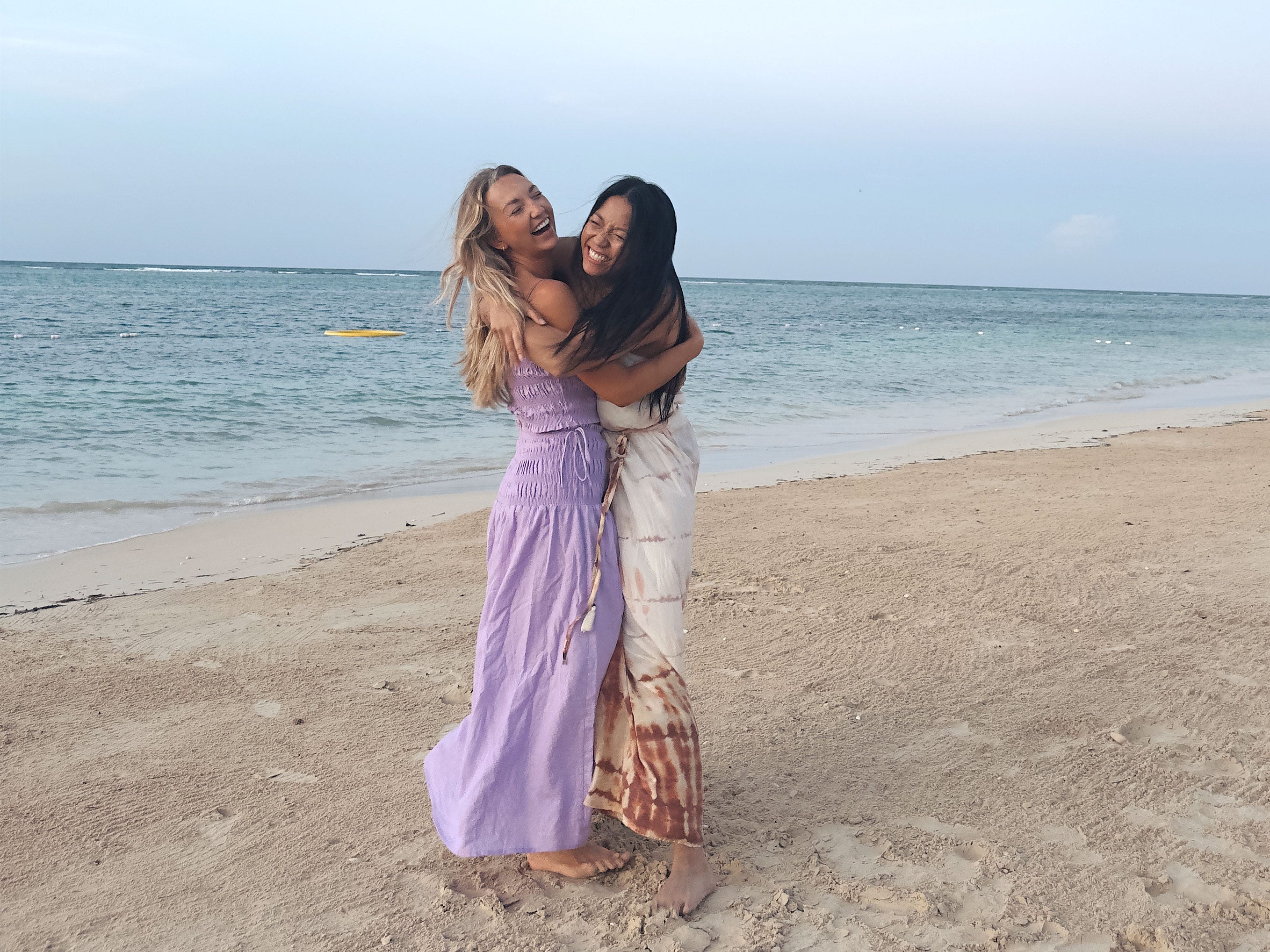 Chloe and her friend hug on the beach at dusk.