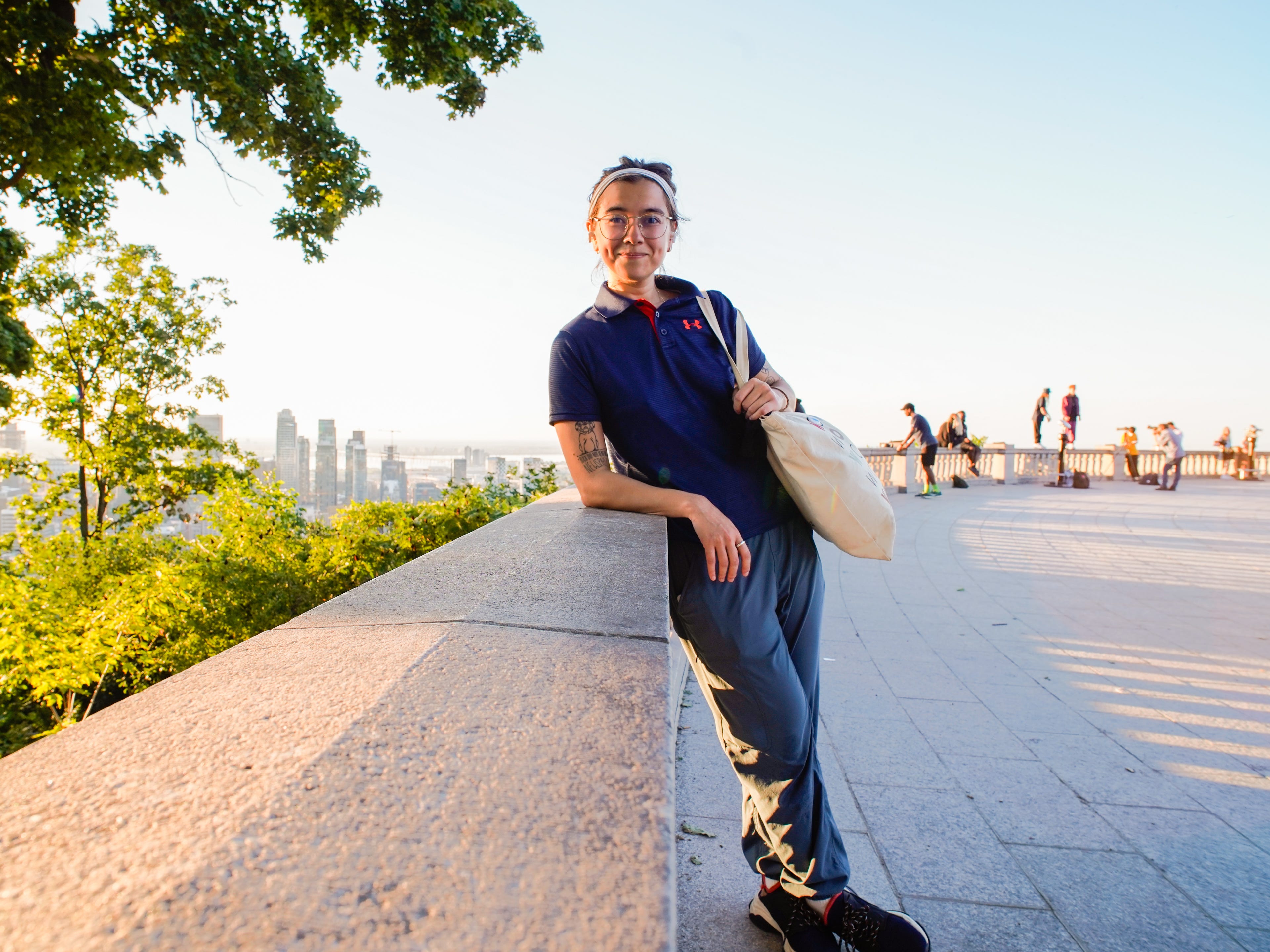 The author poses in a polo with a tote bag at a view point of the city from the top of Montreal