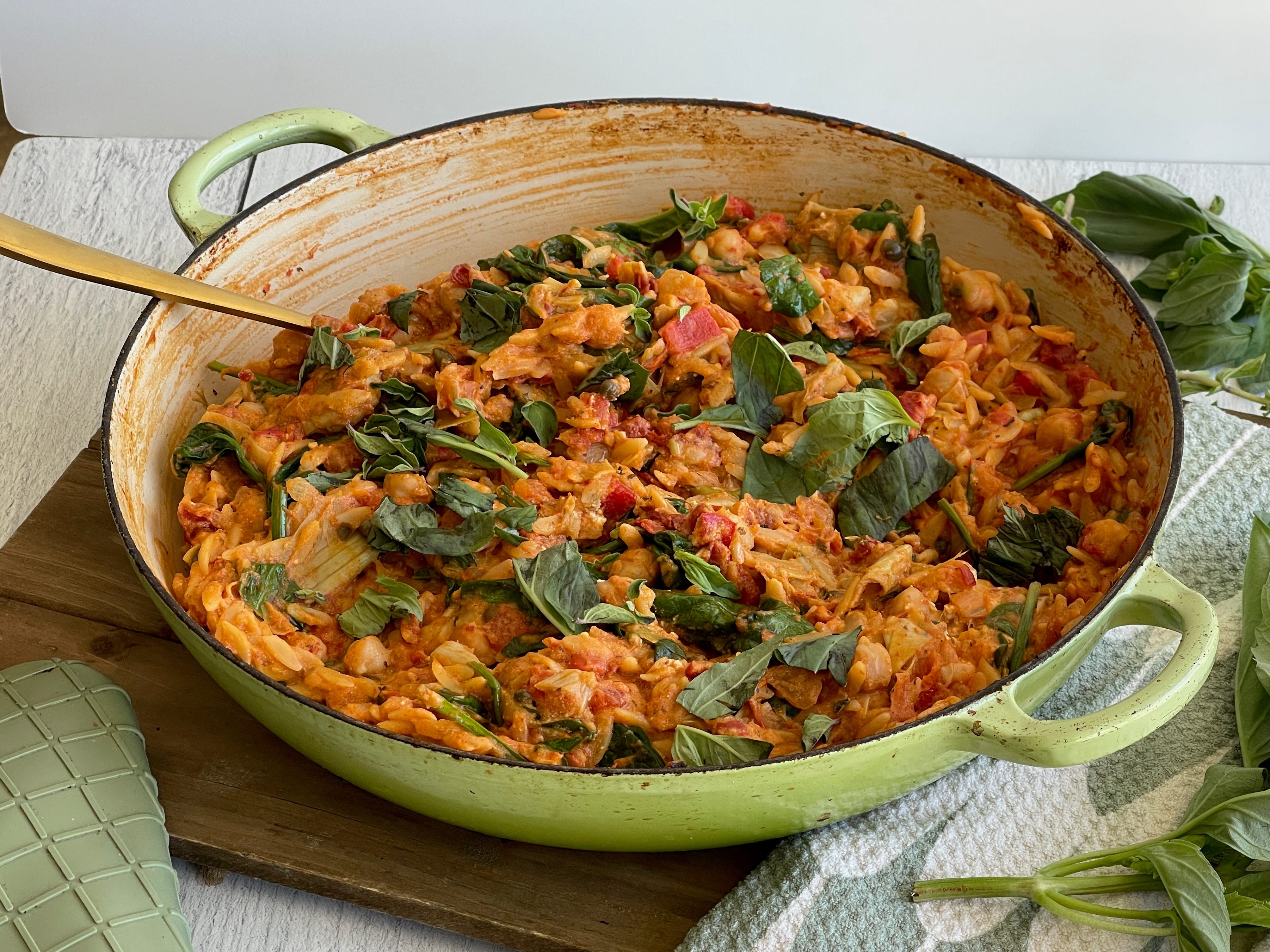 Cooked orzo in a pan garnished with basil leaves on a kitchen table.