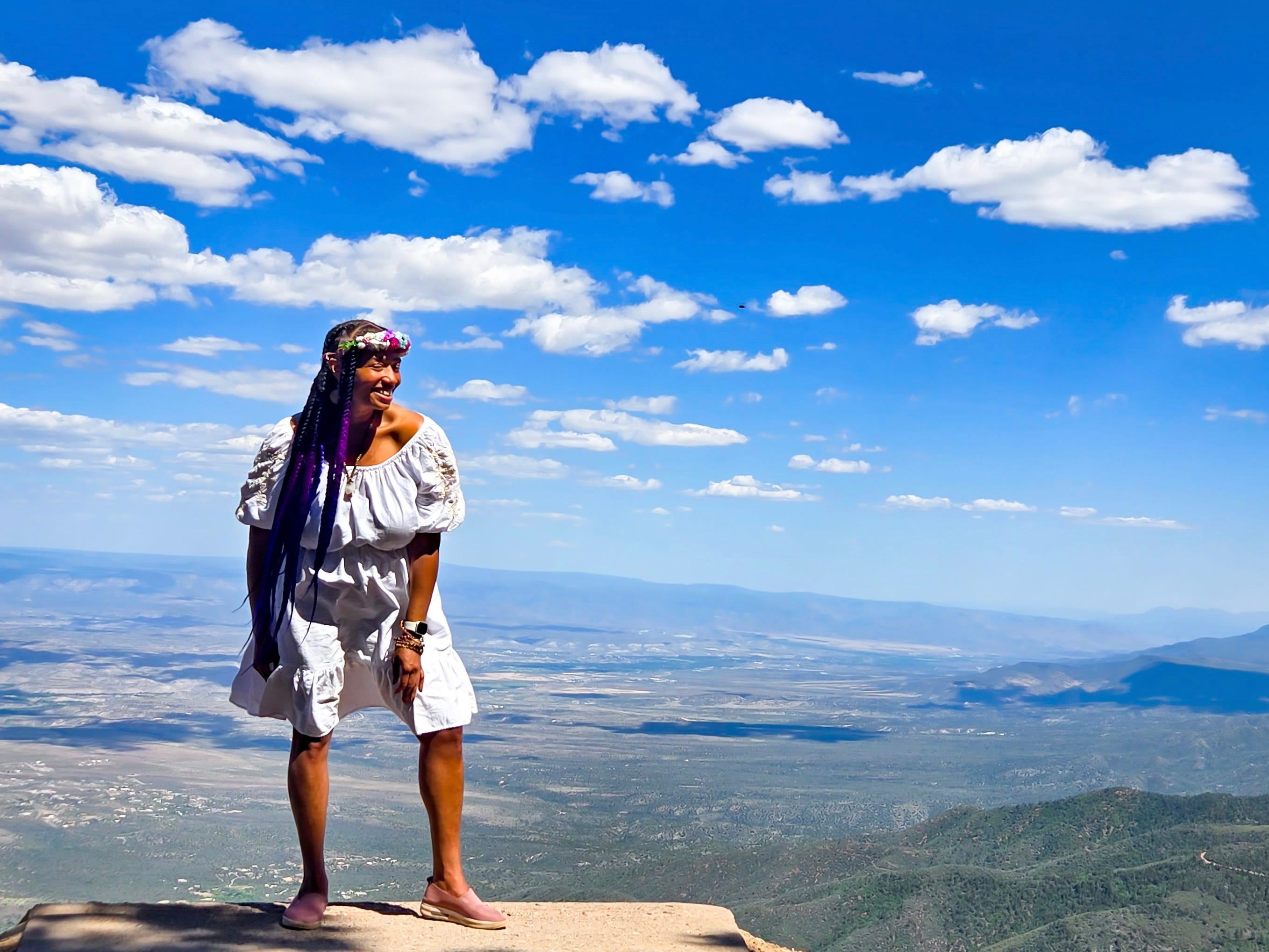 The author standing in front of a blue sky and mountain view wearing a white dress.