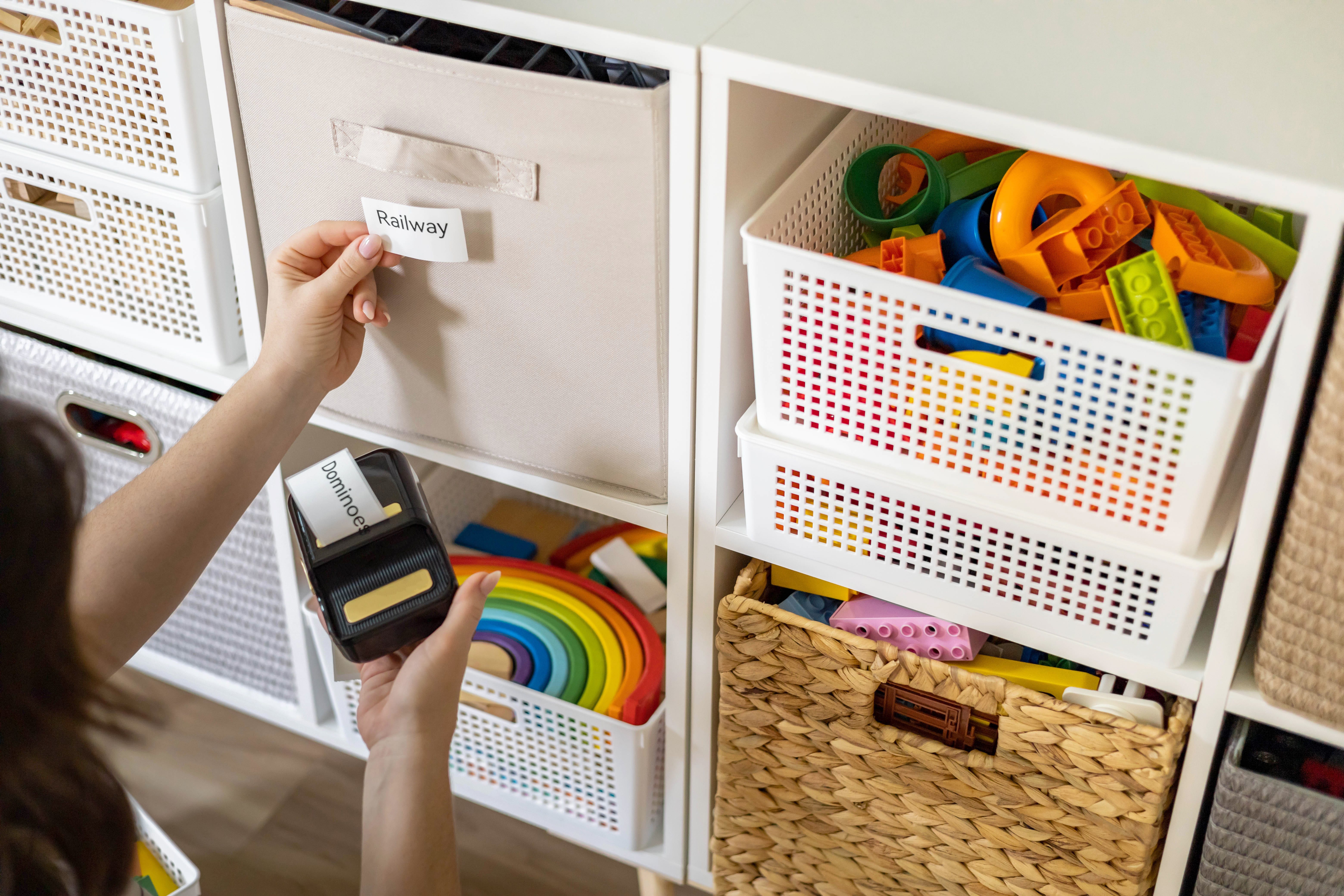 A woman using a label maker to mark bins of toys.
