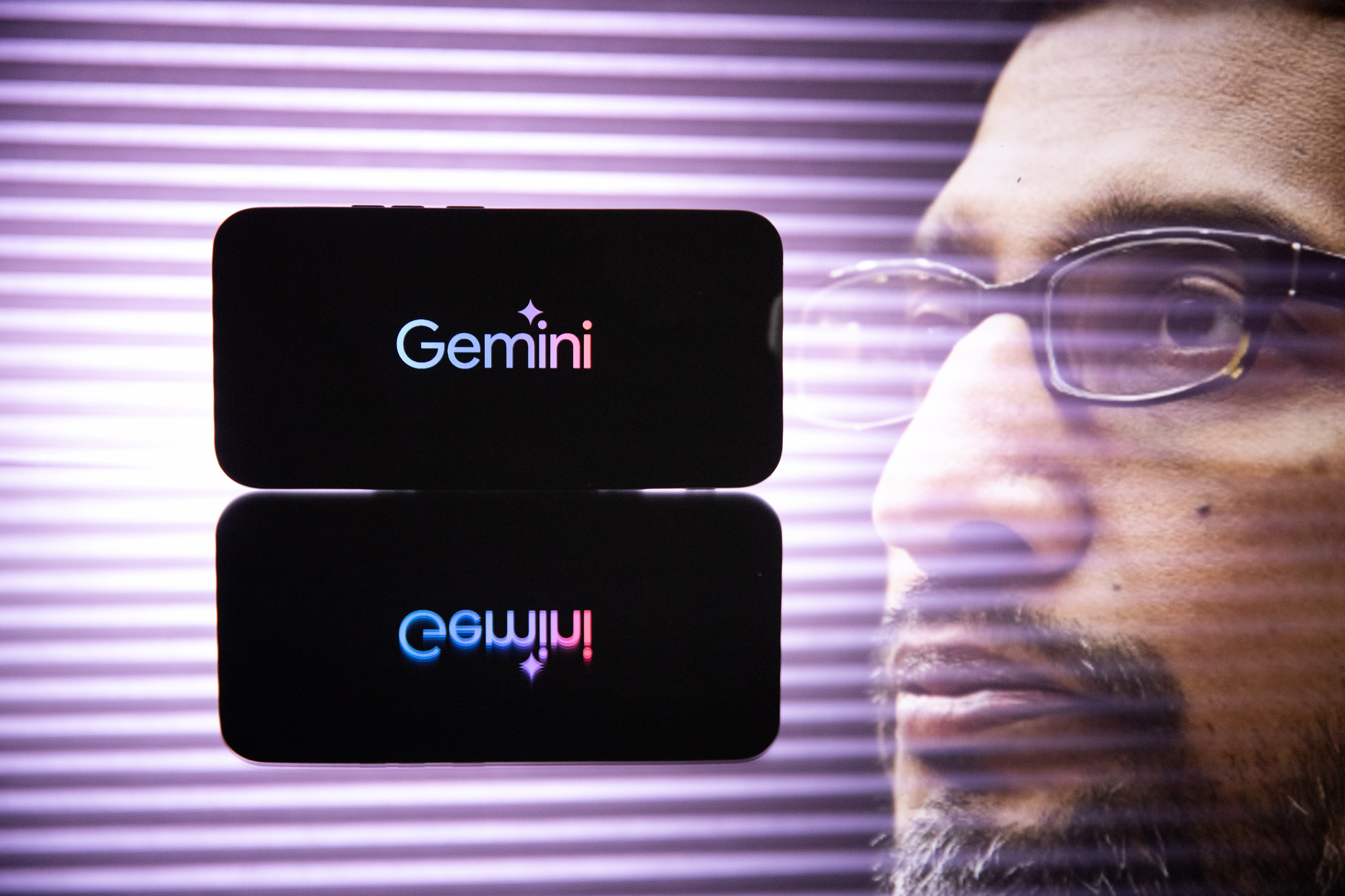 Double exposure photograph of a telephone displaying the Gemini artificial intelligence logo and Google chief executive Sundar Pichai in front of a purple lit background at Kerlouan in Brittany in France on June 7 2025.