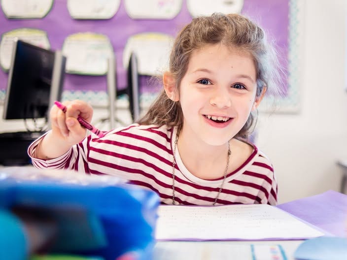 The author's child at school, smiling and holding a crayon