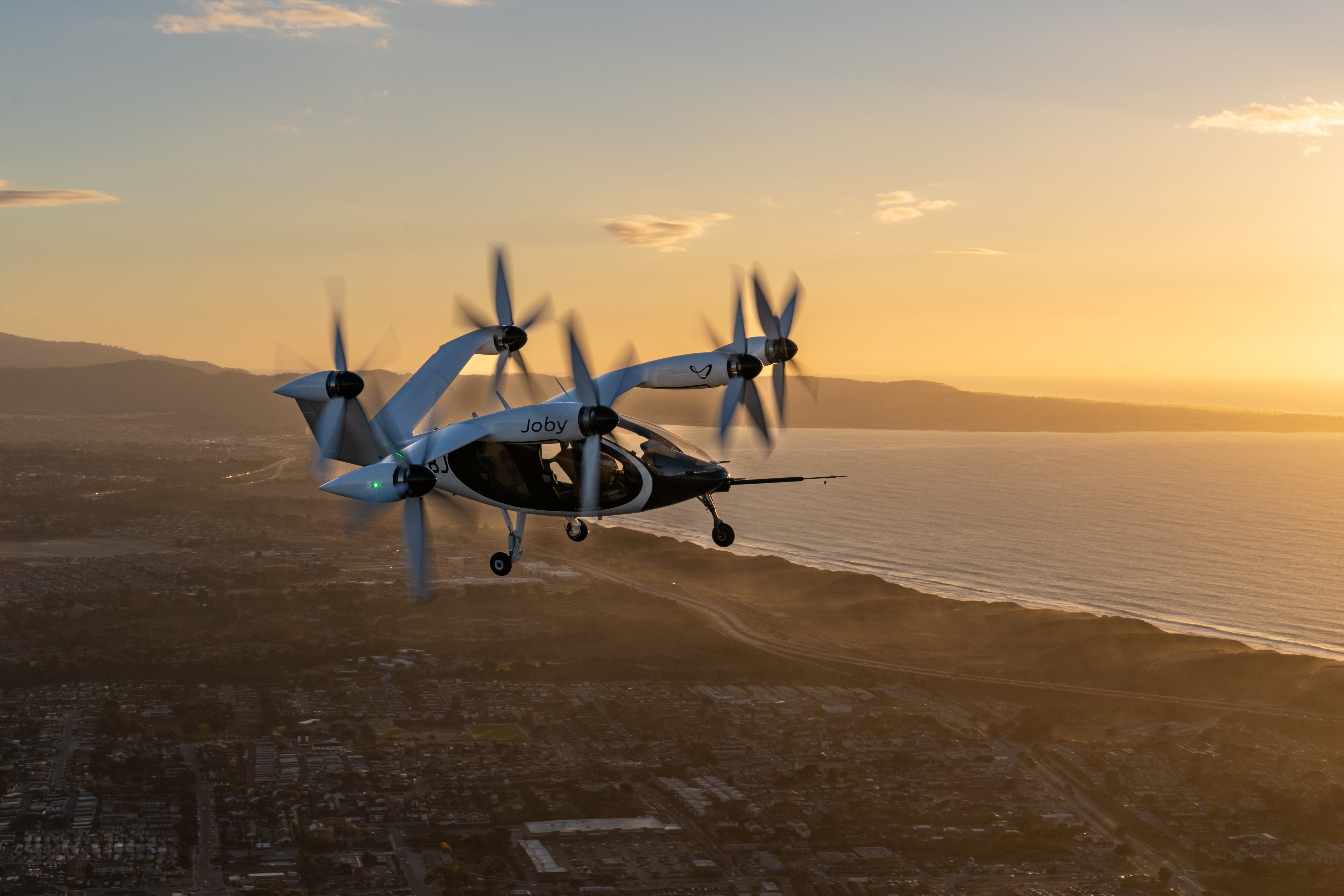 A Joby air taxi in flight at sunset with the ocean in the background