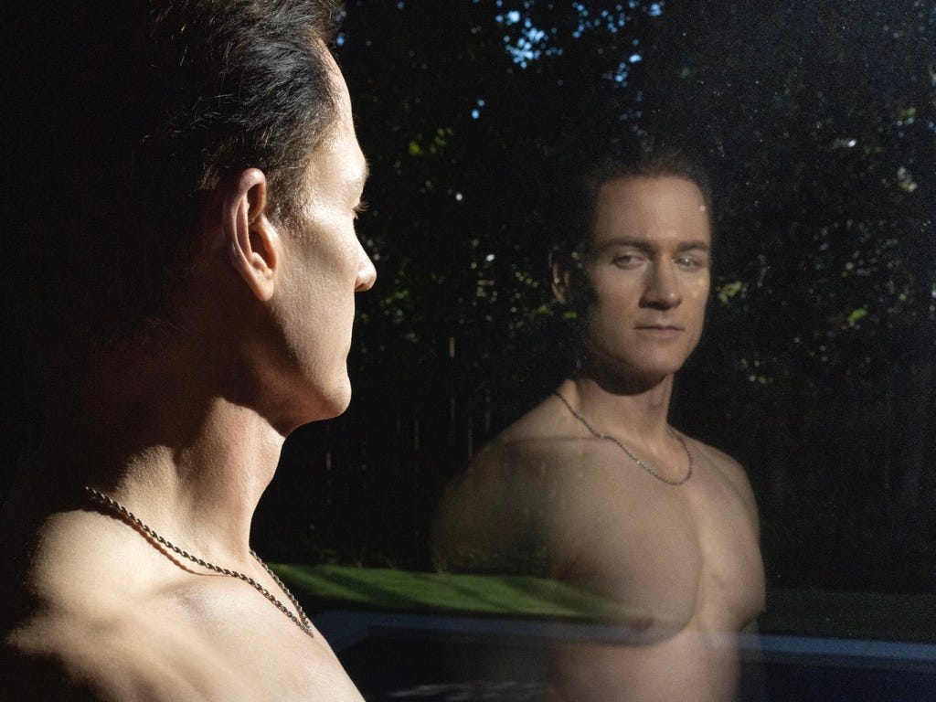 Bryan Johnson looking at his reflection in a window while shirtless.
