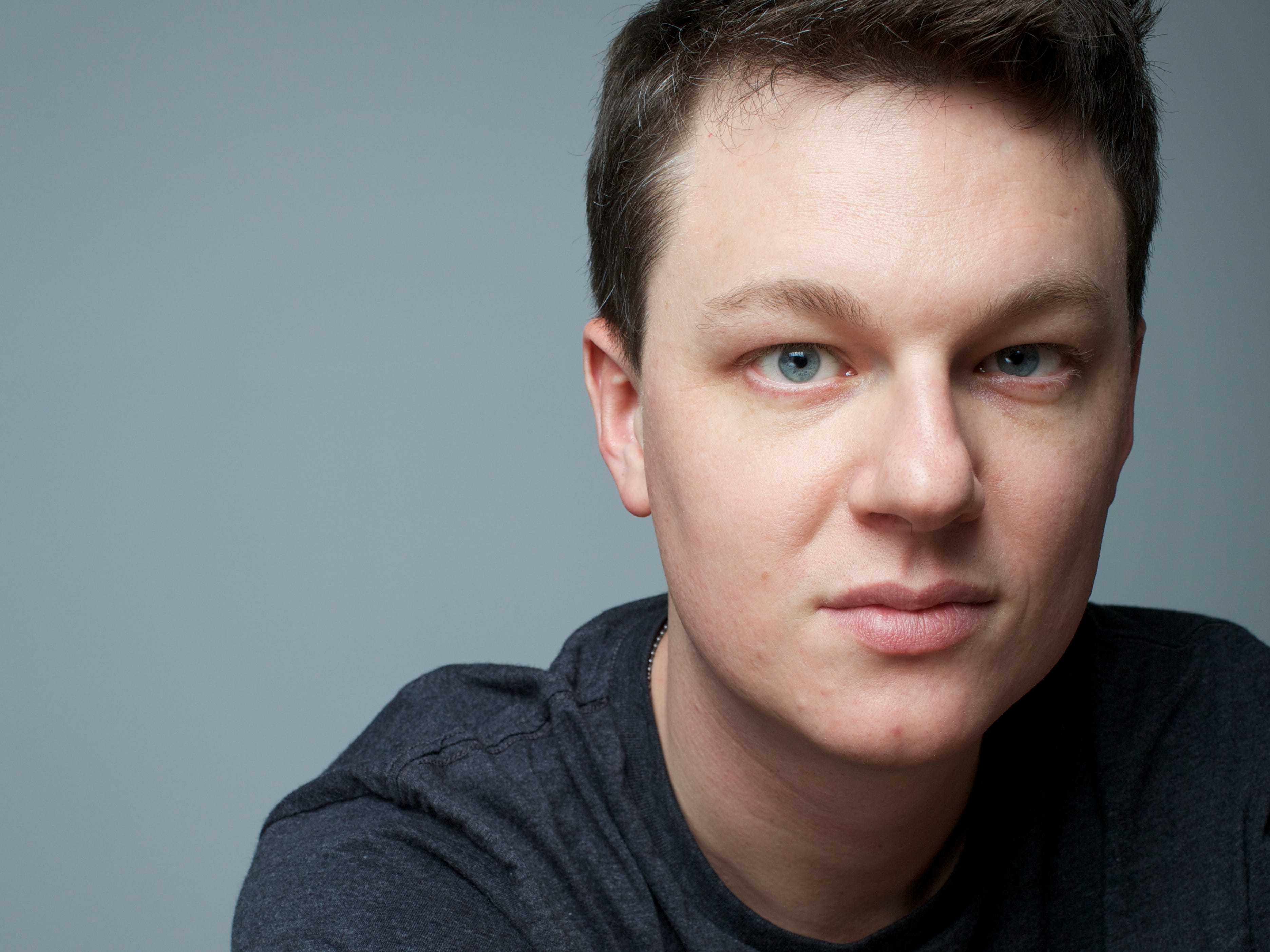 A headshot of NetBox Labs' Kris Beevers wearing a grey shirt and sitting in front of a grey background.