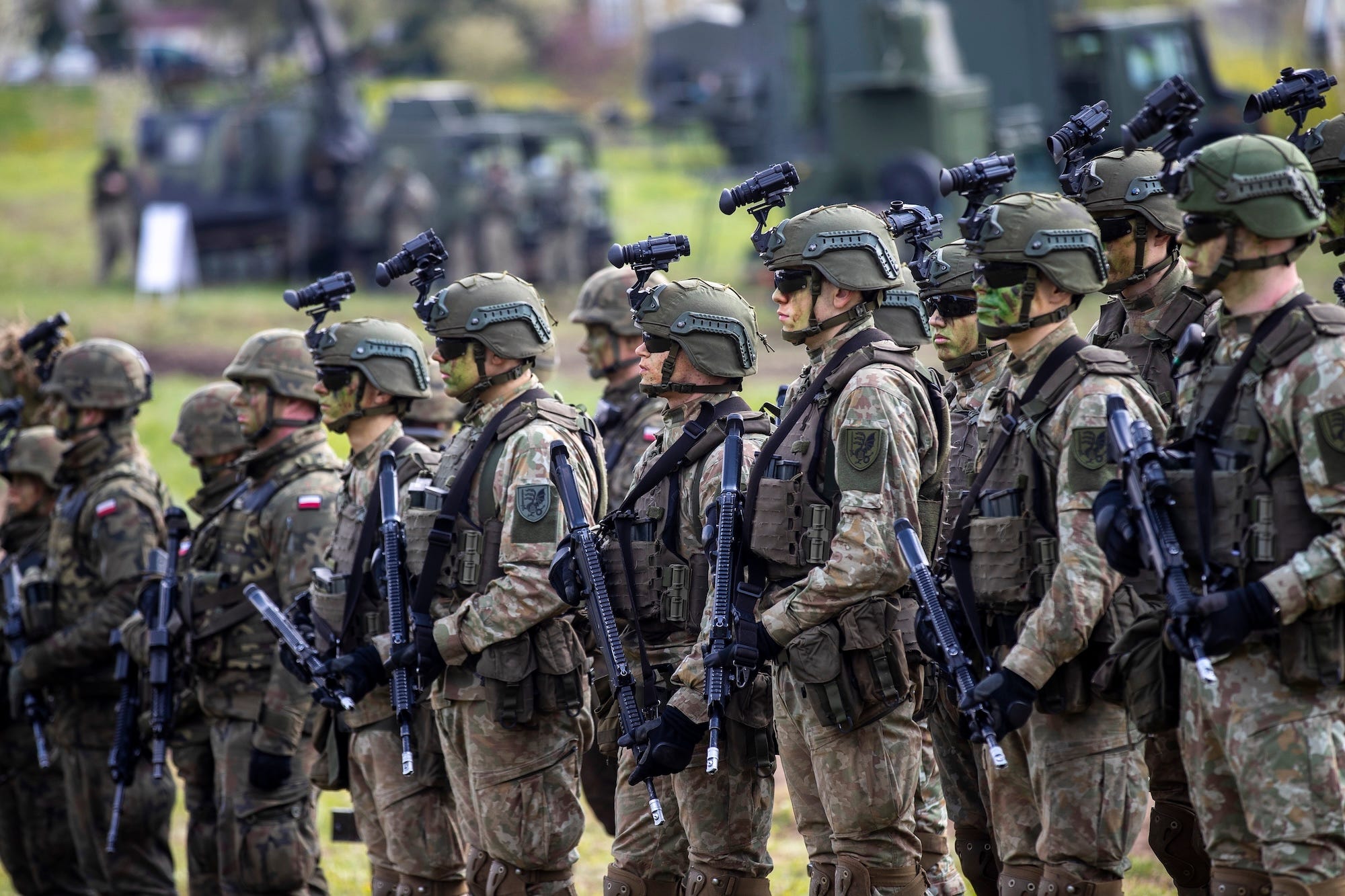 Soldiers in camouflage gear and helmets stand holding firearms and wearing sunglasses.