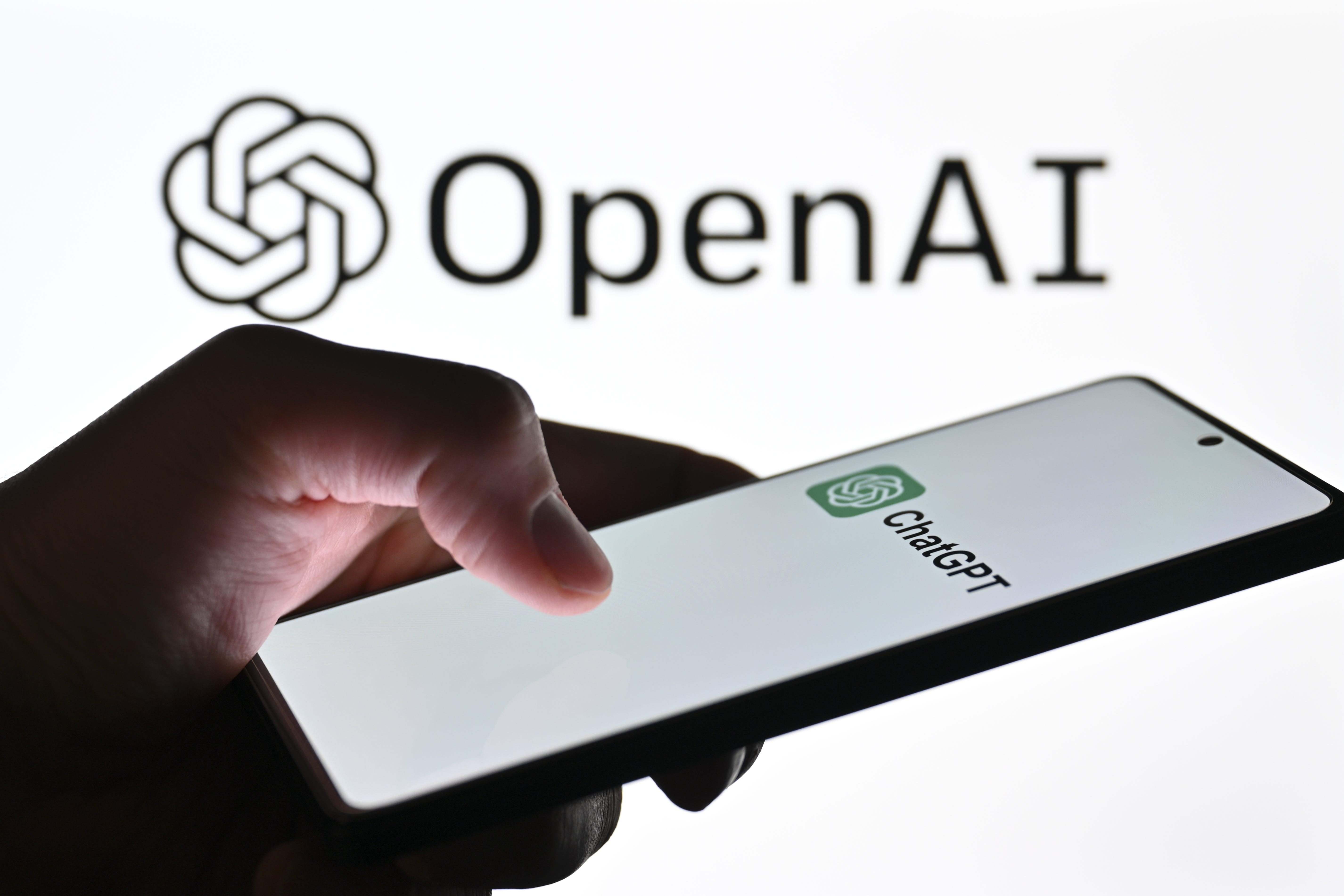 in this photo illustration, the logo of 'ChatGPT' is displayed on a mobile phone screen in front of a computer screen with the logo of 'OpenAI'