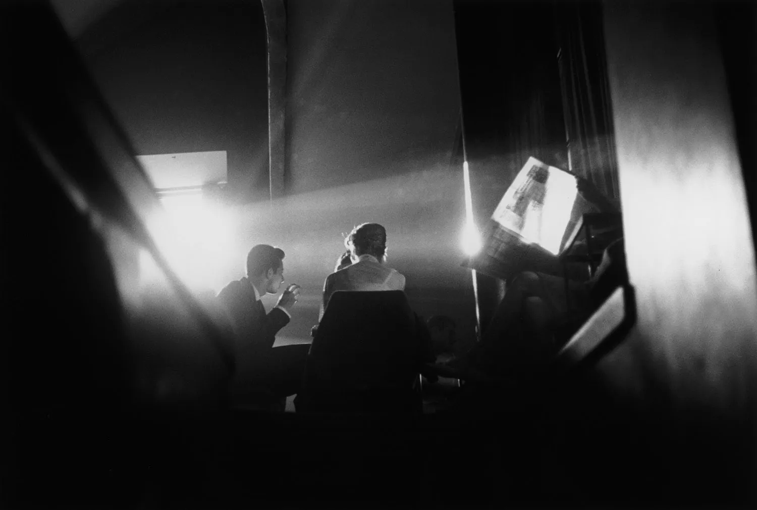 Two people are silhouetted in a shaft of light as they sit in chairs in a cafe.