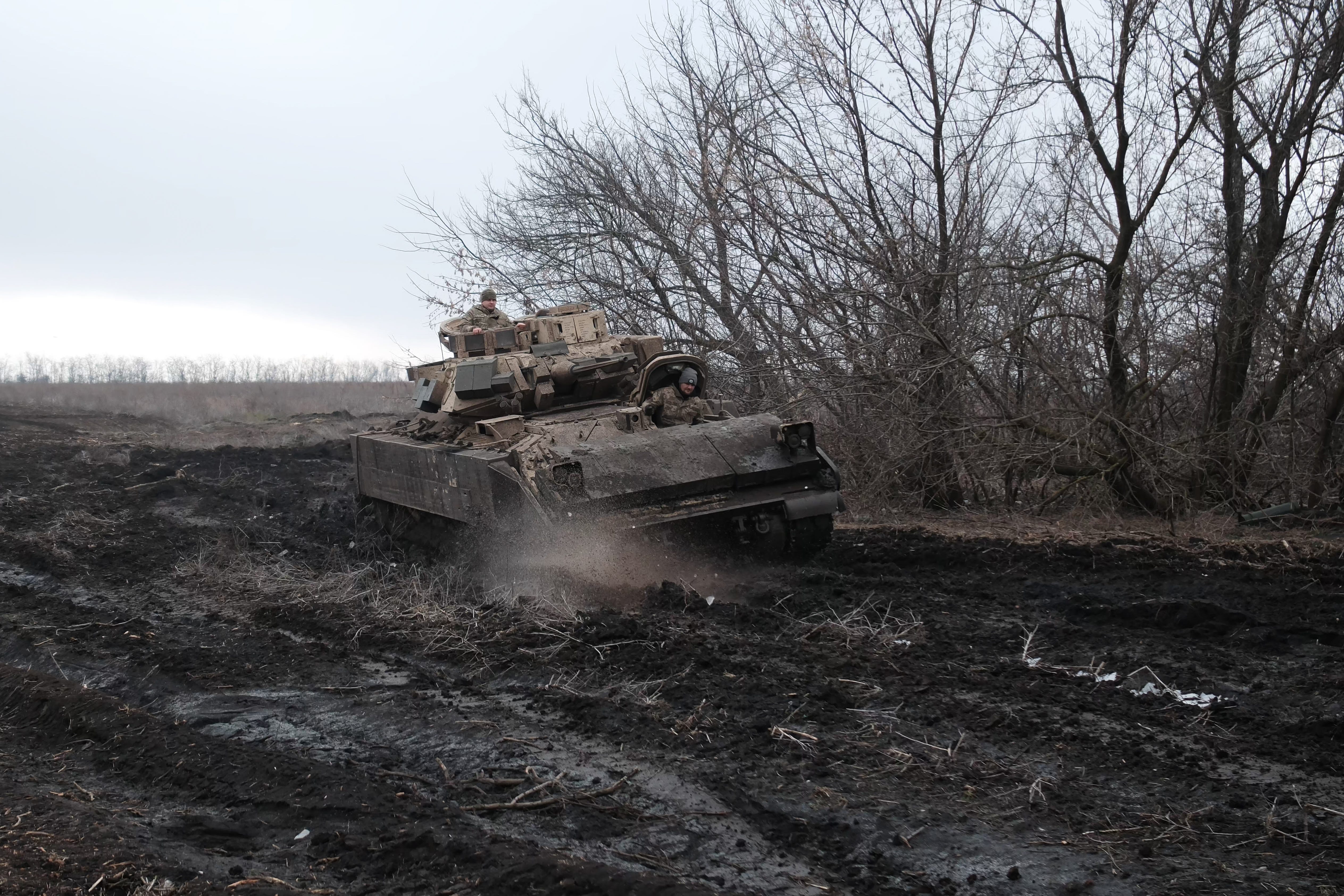 A US-provided Bradley infantry fighting vehicle driving in deep mud surrounded by dead trees in Ukraine.