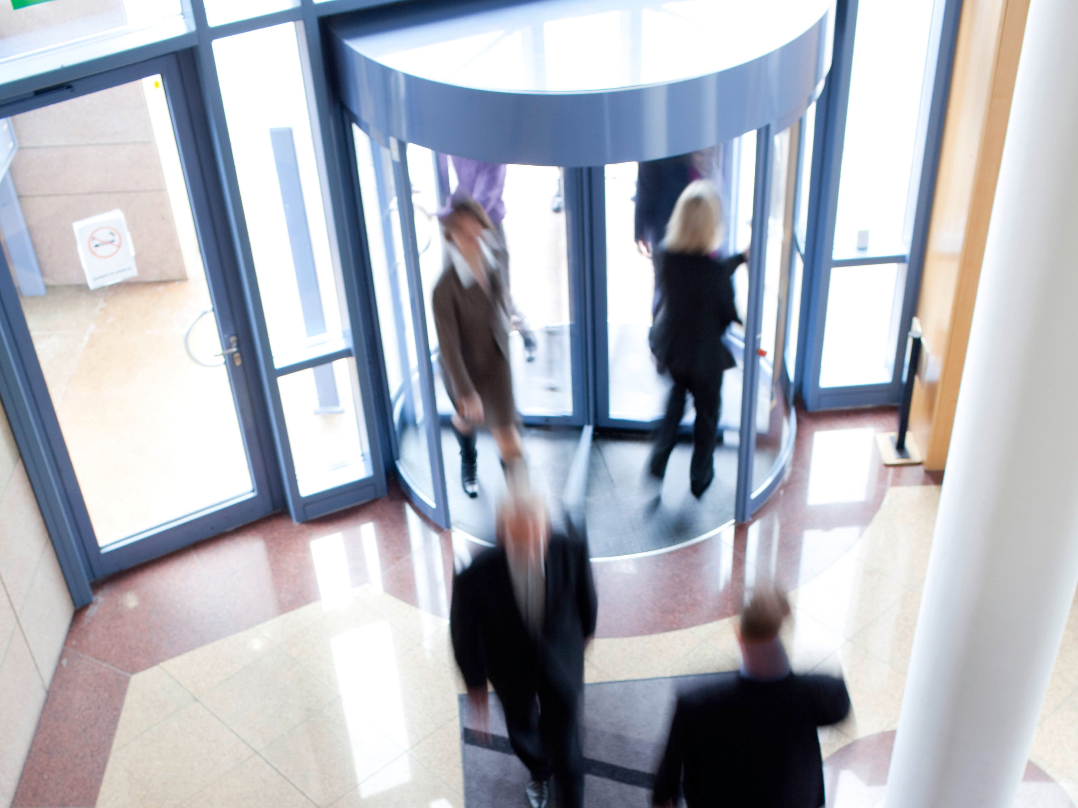 six people go in and out of an office through a revolving door
