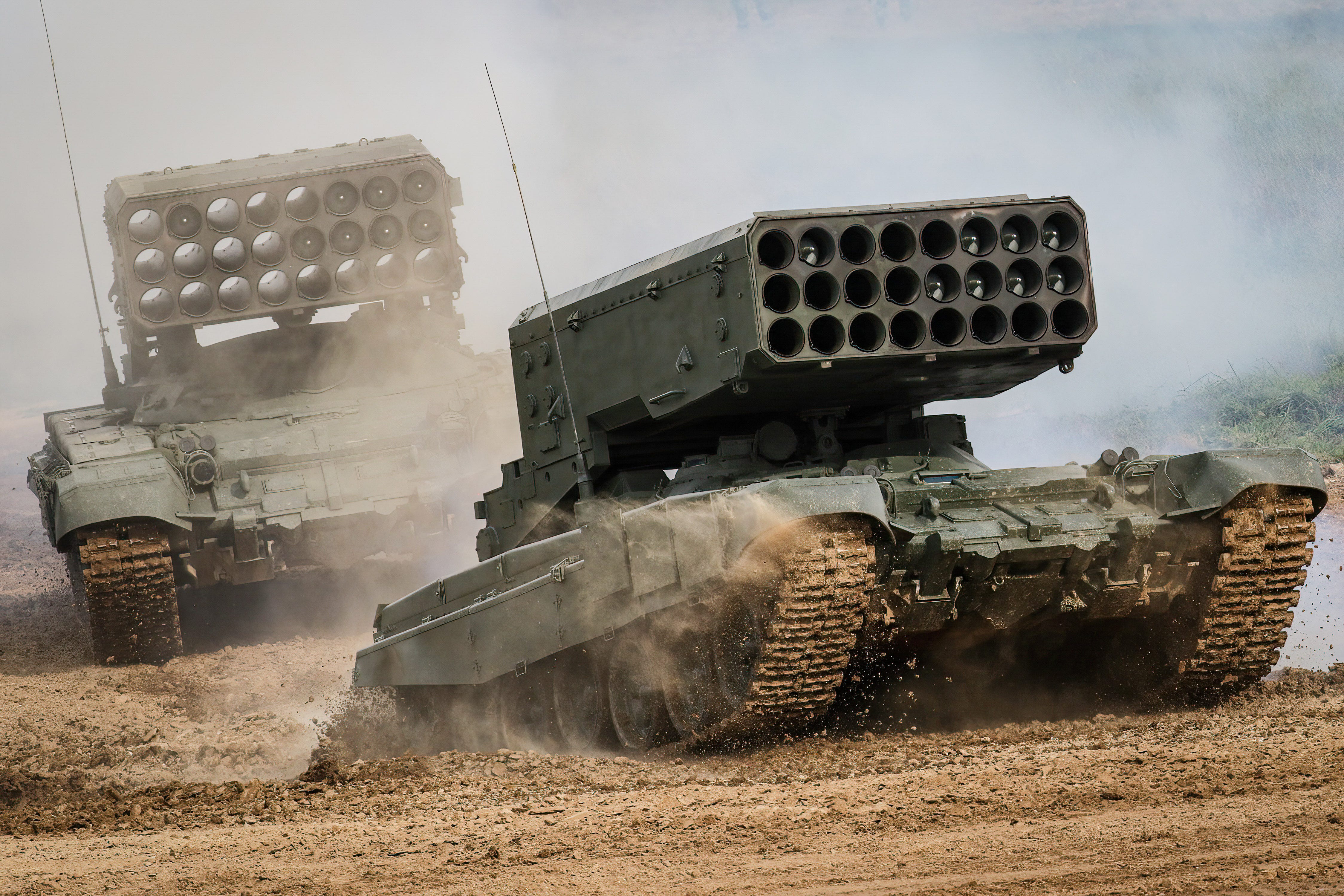 Two Russian TOS-1A multiple-launch rocket systems navigate muddy terrain.