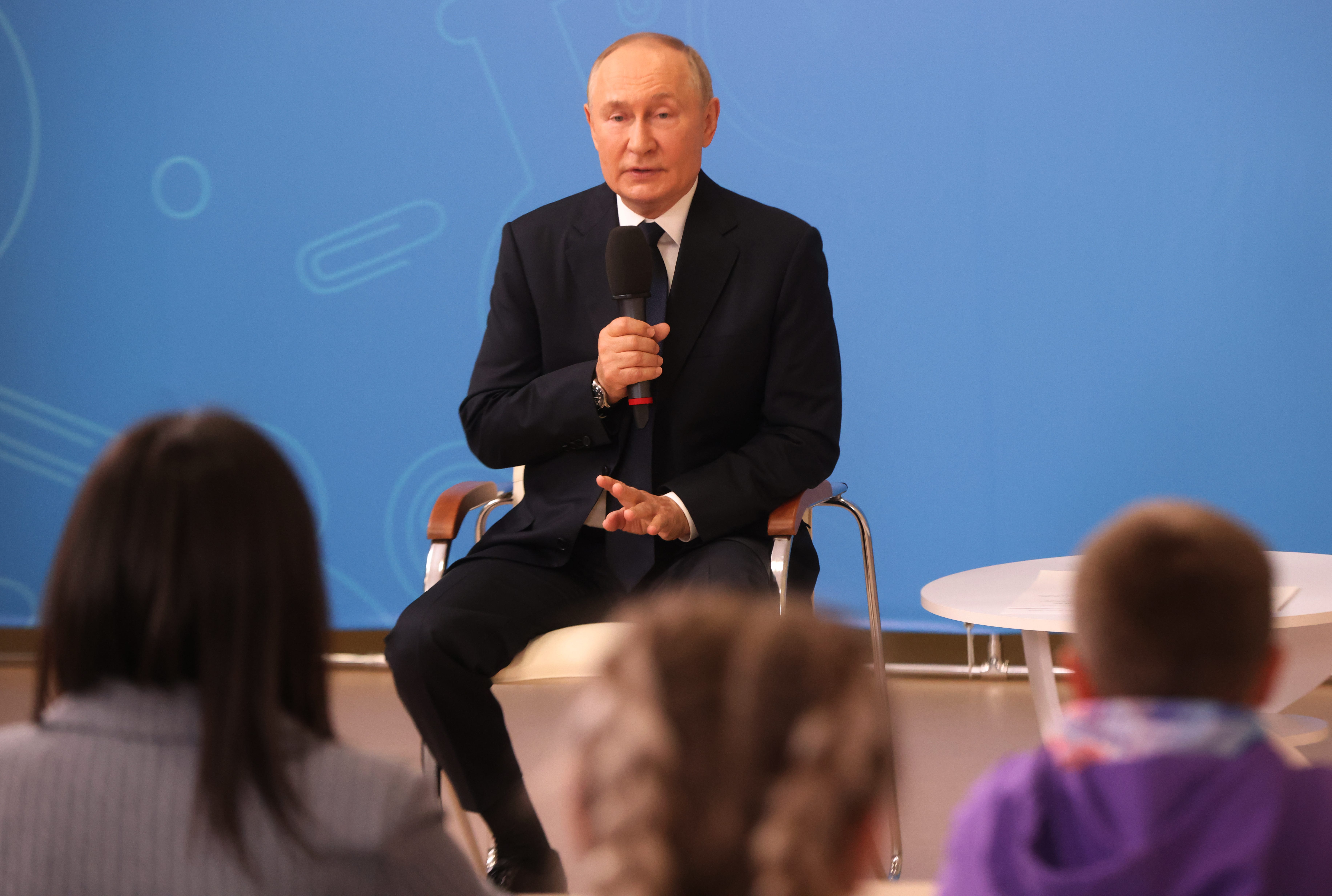 Putin holds a microphone and speaks to students while visiting a school in September 2024.