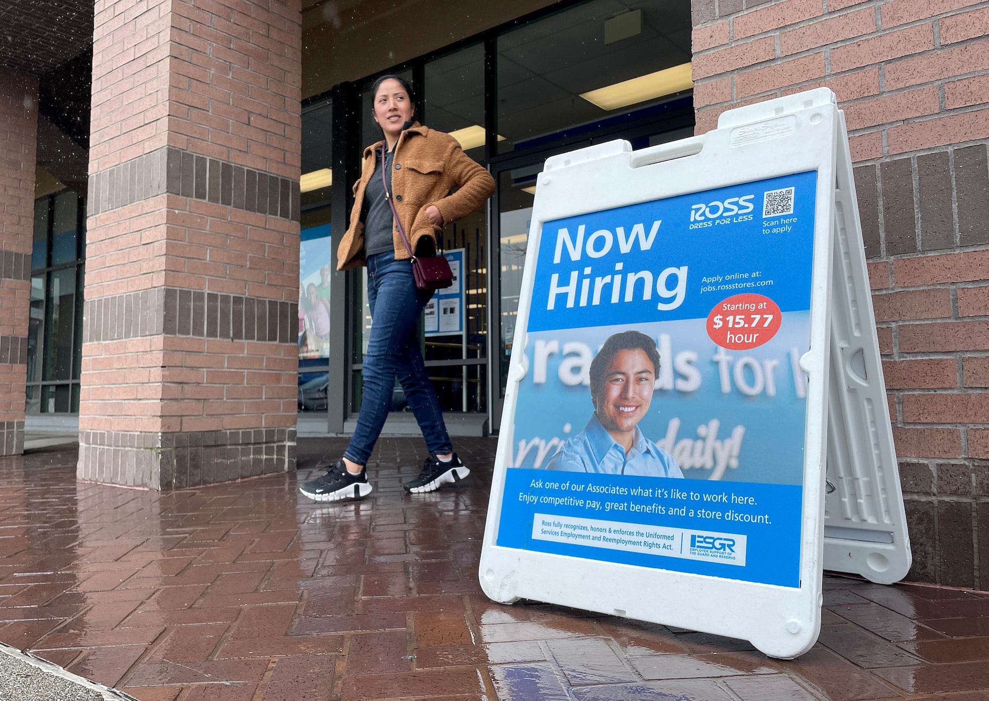 A customer walks by a now hiring sign