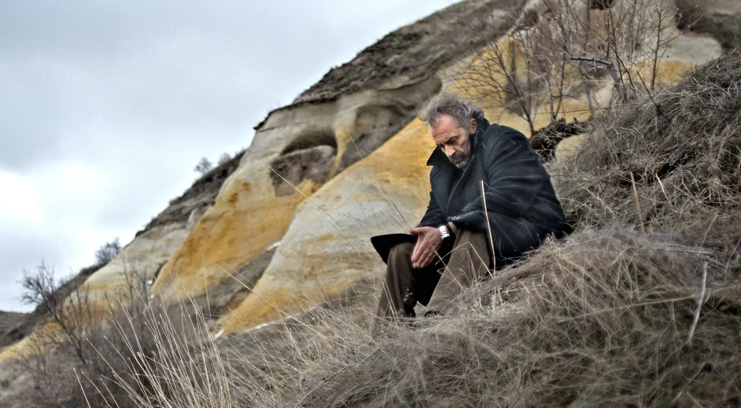 A man in a coat on a rocky bleak landscape.