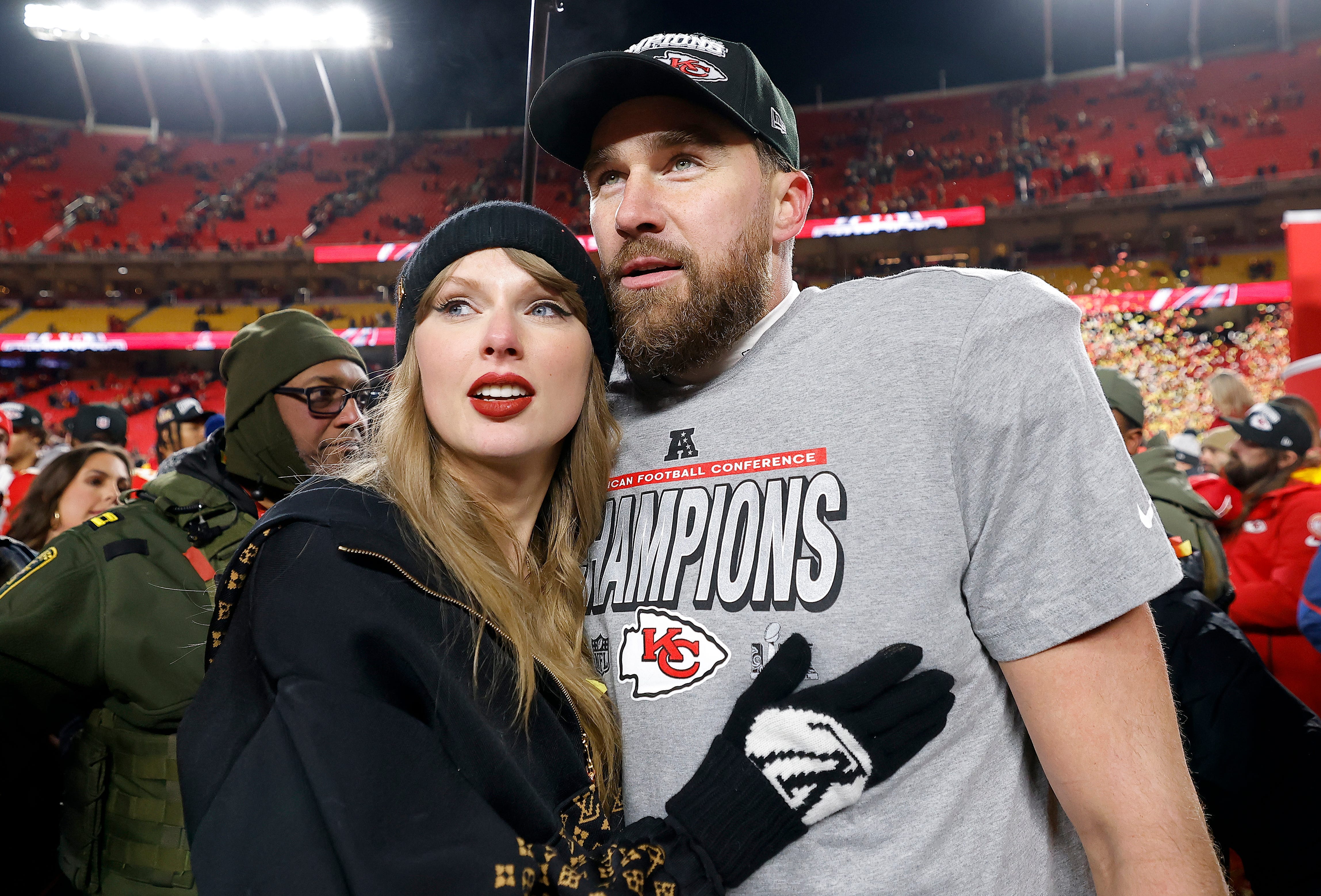 Taylor Swift (left) touching Travis Kelce's (right) chest as they both look toward their right at Arrowhead Stadium.