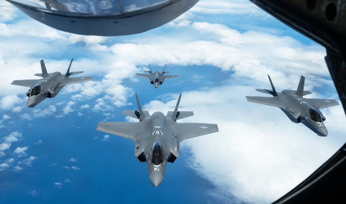 Four F-35 fighter aircraft fly above a cloudy blue sky.