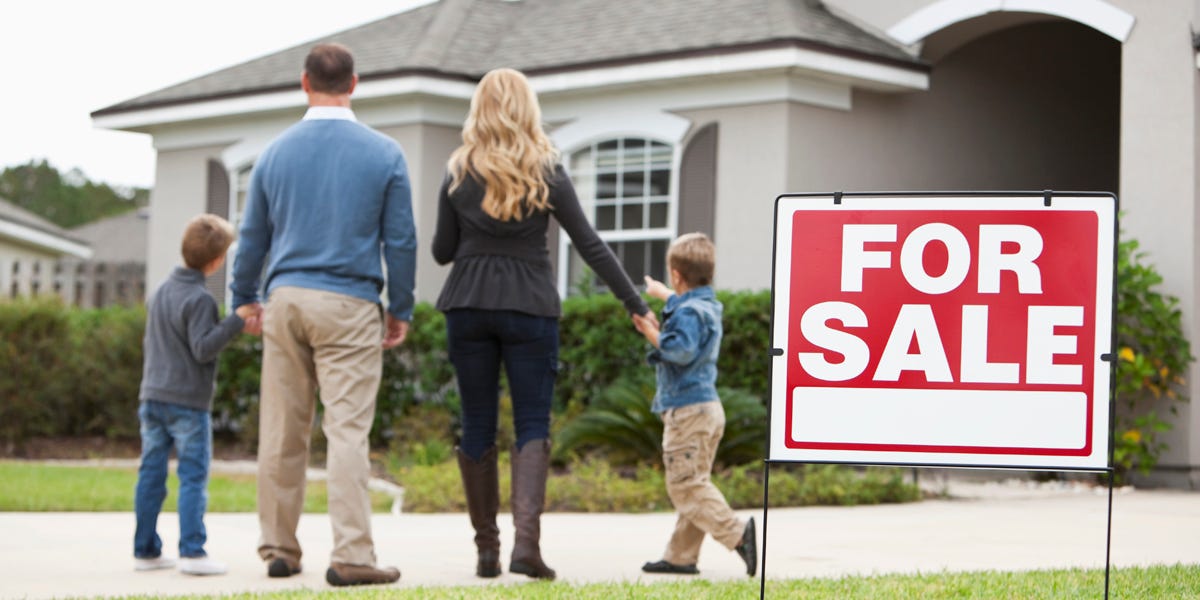 A young family in front of a house with a for-sale sign that could be purchased with a subprime mortgage.