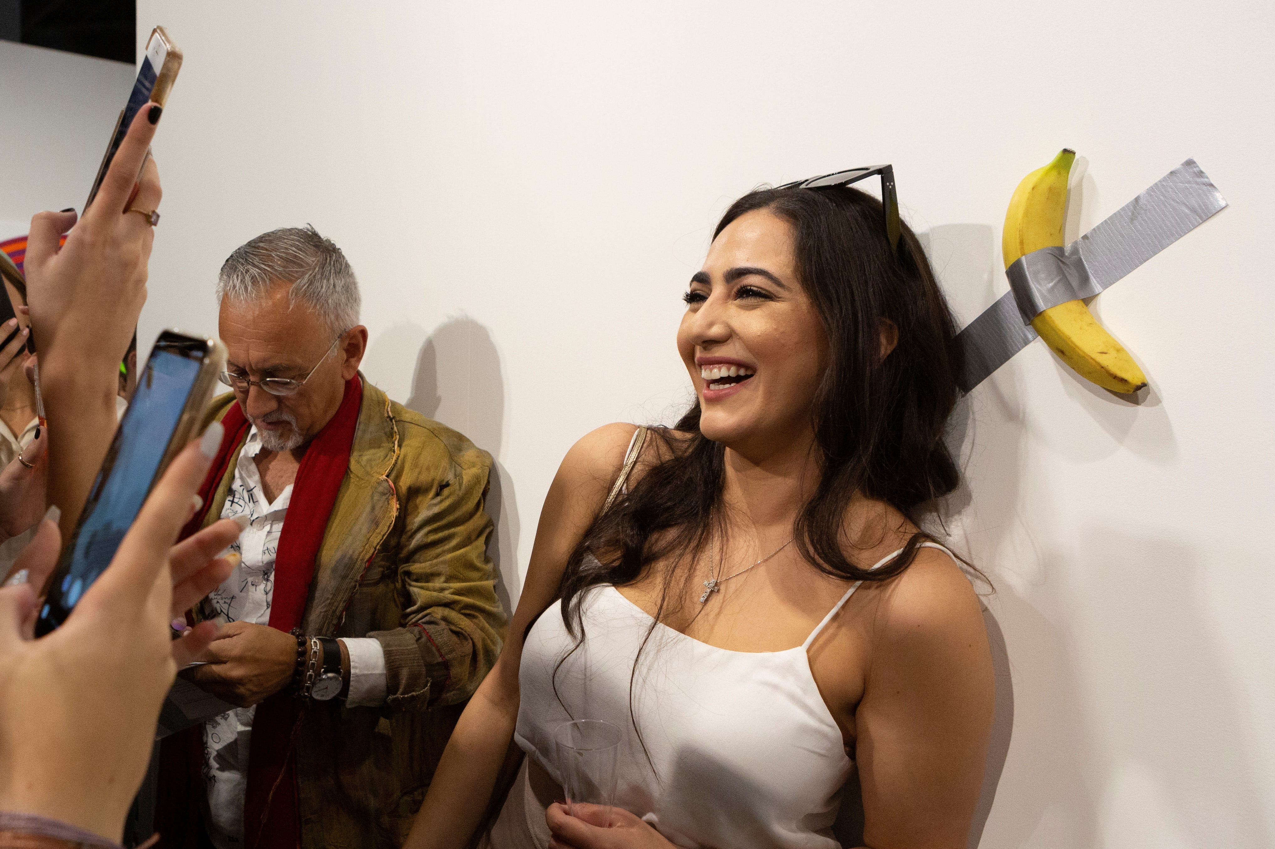 A woman poses for a photo next to a banana attached with duct-tape that replaces the artwork 'Comedian' by the artist Maurizio Cattelan, which was eaten by David Datuna, in Miami Beach, Florida, December 7, 2019.