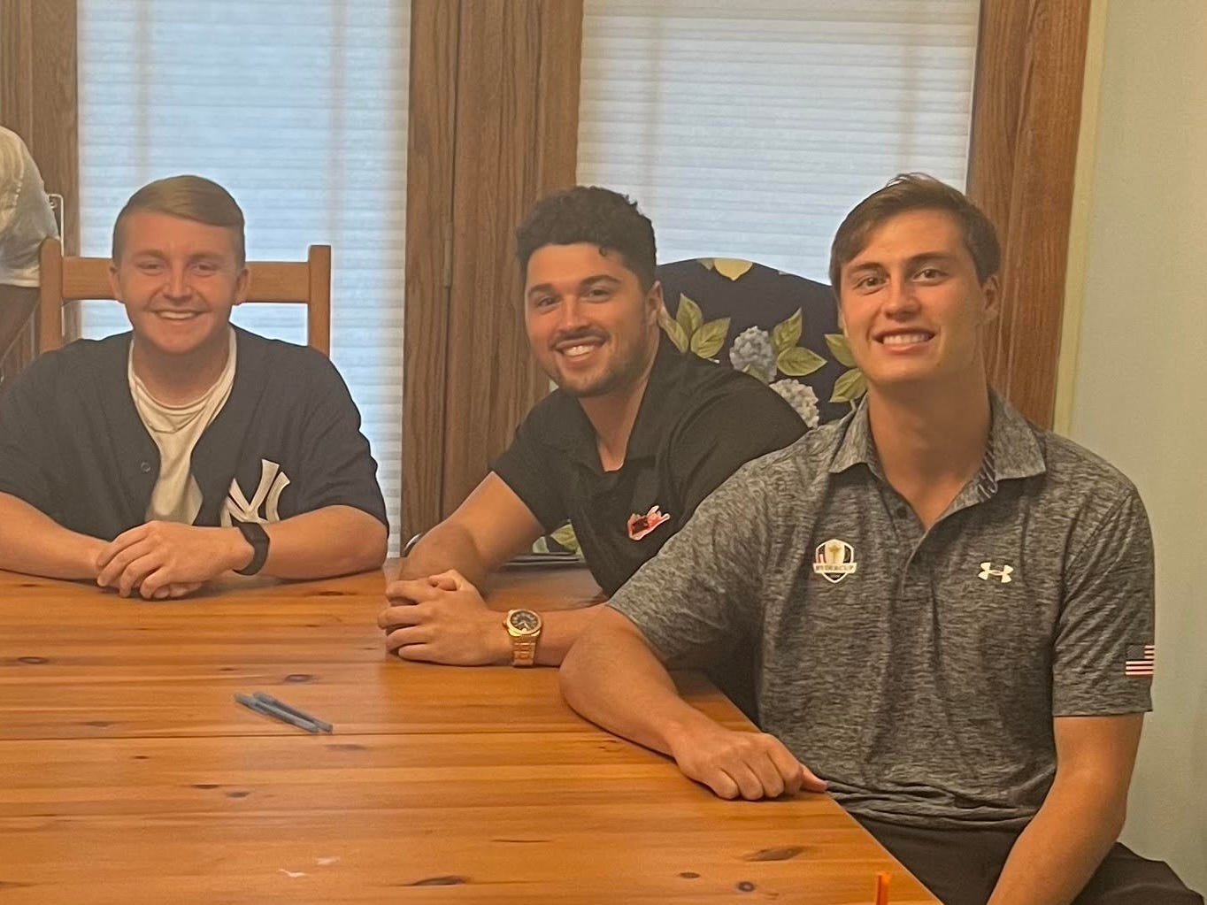 Three young men sit at a dinner table, smiling at the camera.
