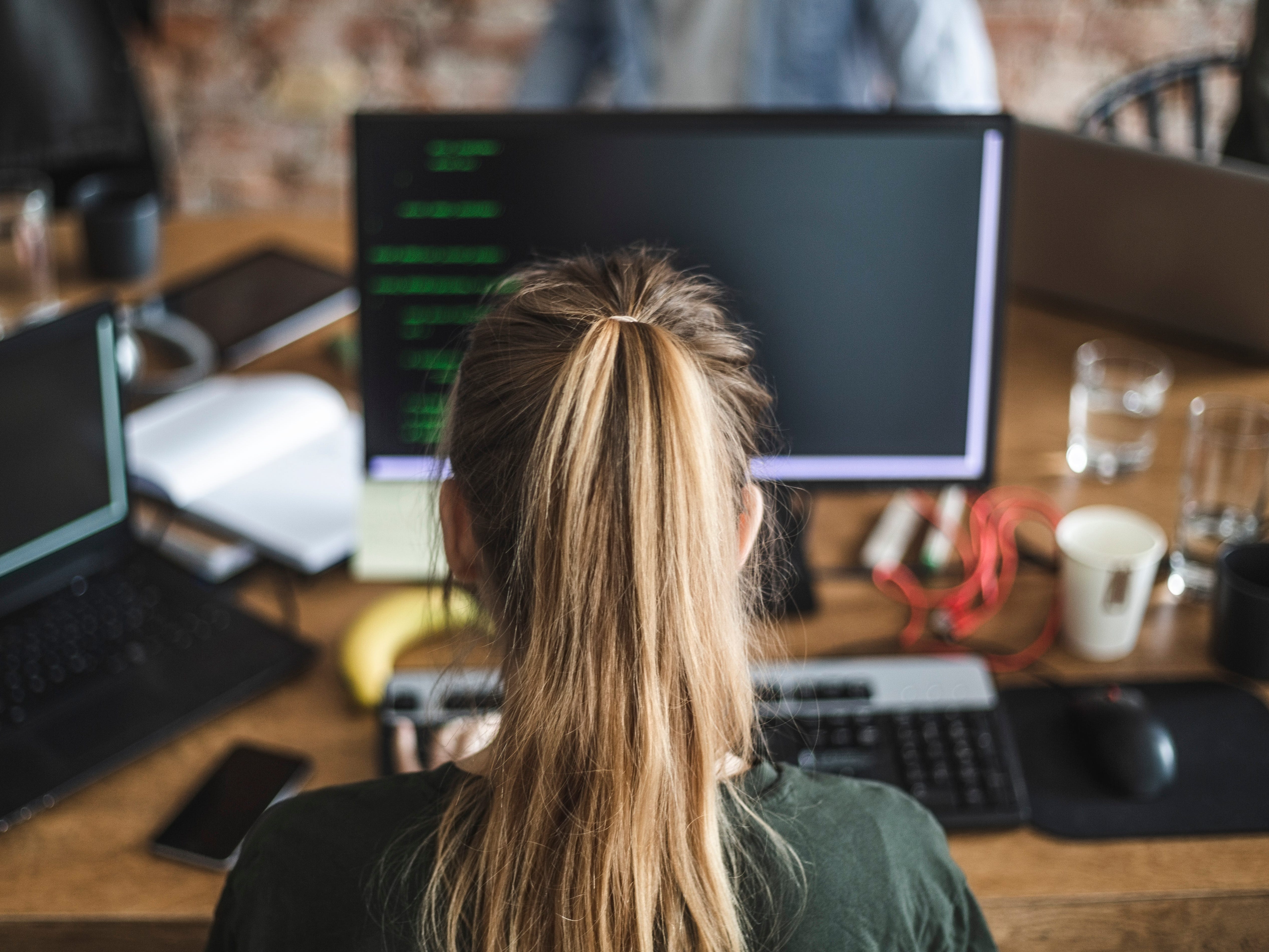Blond female programmer coding over computer in startup company - stock photo