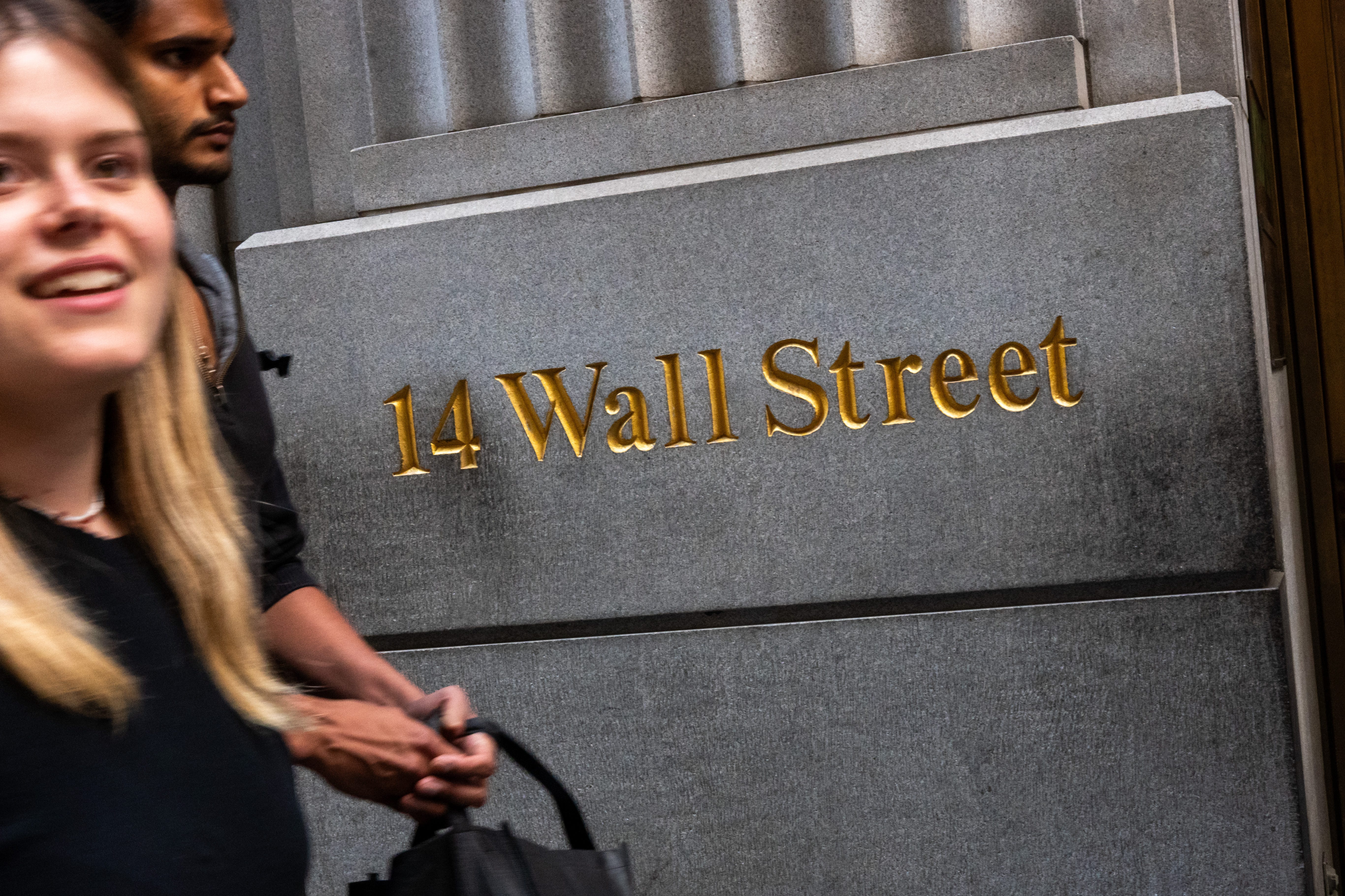 People walk by a Wall Street sign