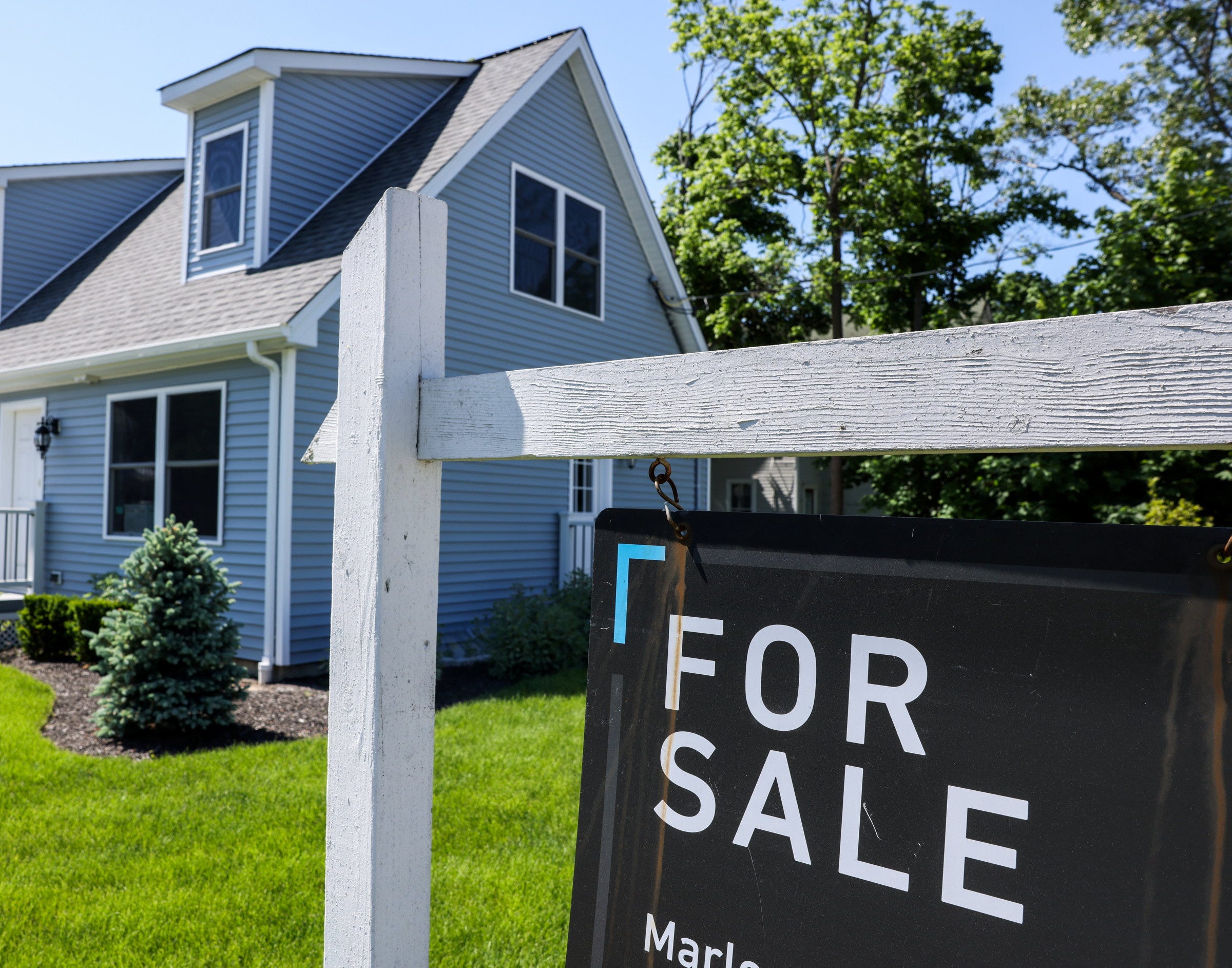 A large blue home with a for sale sign in front of it.