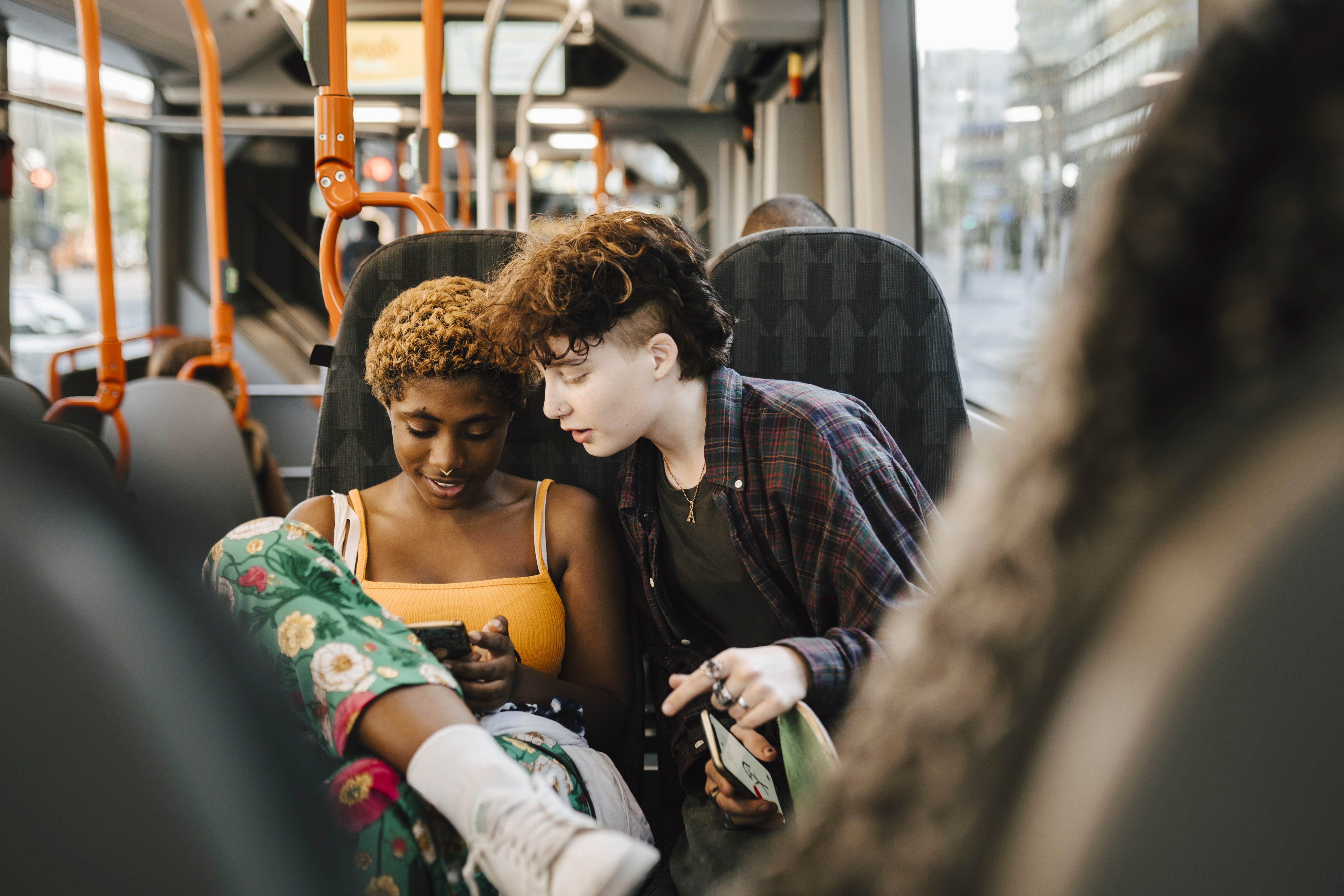 Two teenagers look at a phone on a bus.