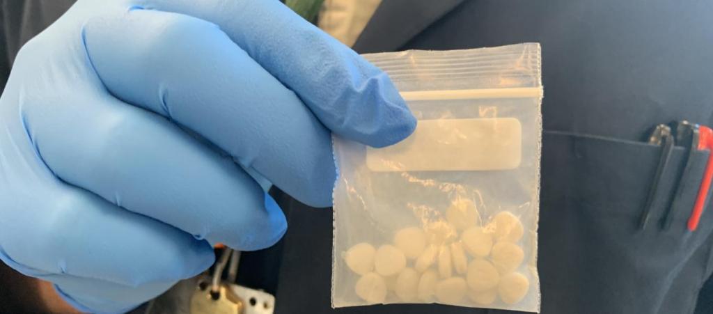A gloved hand holding a bag of nitazene pills.