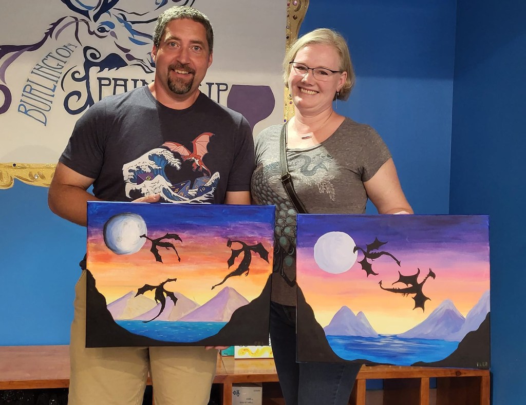 Couple holding paintings of dragons flying past a moon.